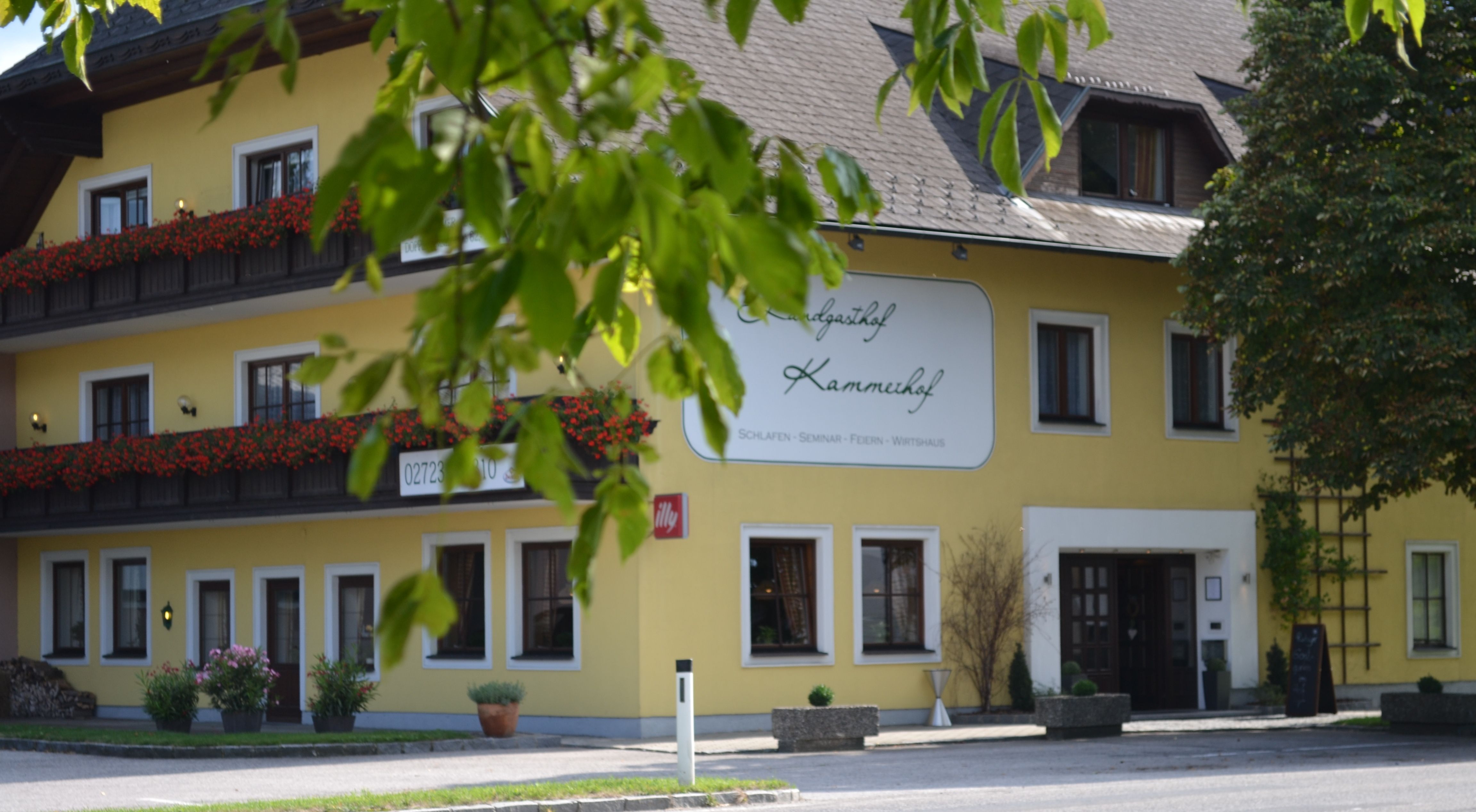 Sárga épület "Landgasthof Kammerhof" felirattal, virágládák és fák az előtérben.