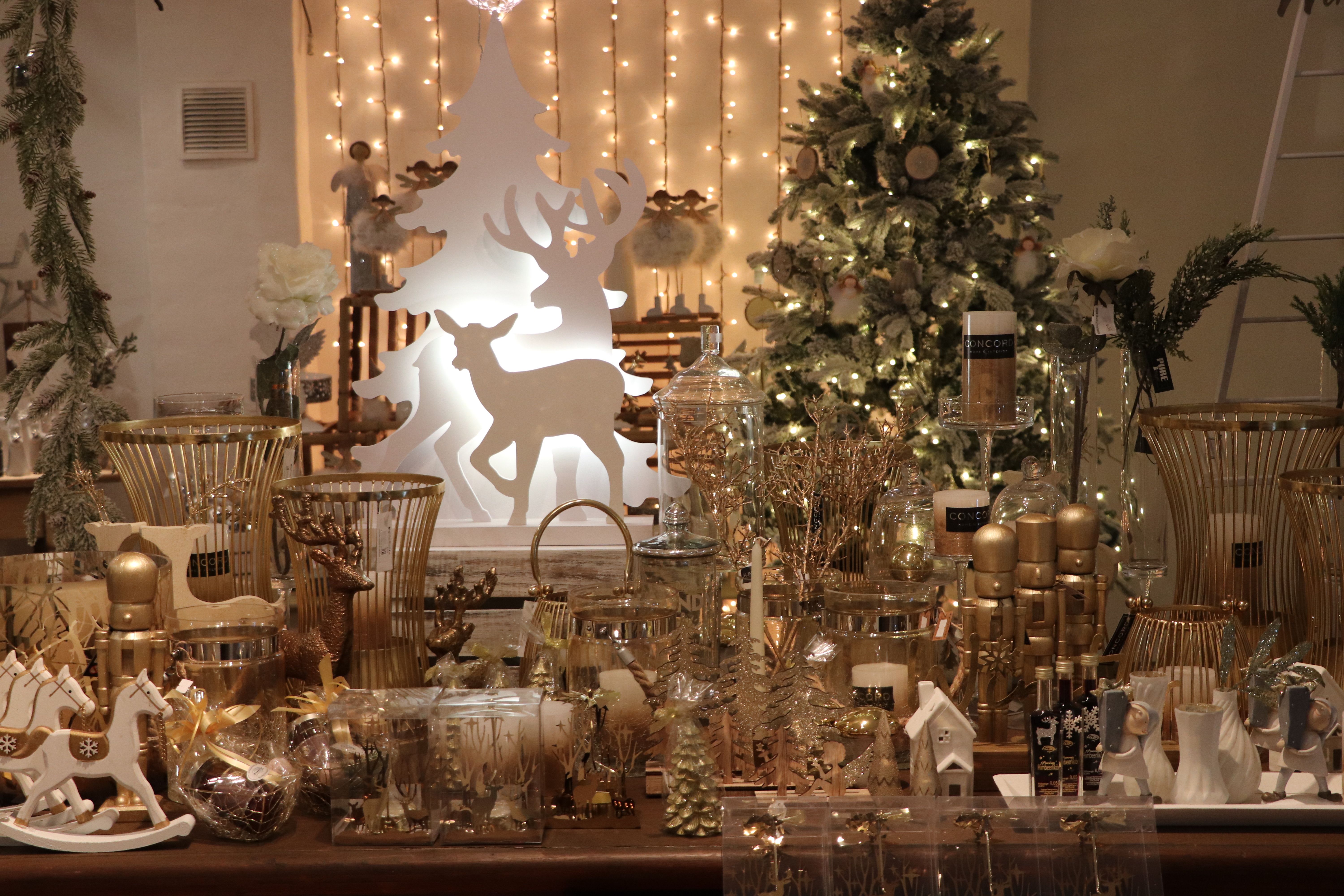 Karácsonyi dekoráció arany és fehér elemekkel, köztük gyertyákkal, rénszarvasokkal és egy karácsonyfával a háttérben.