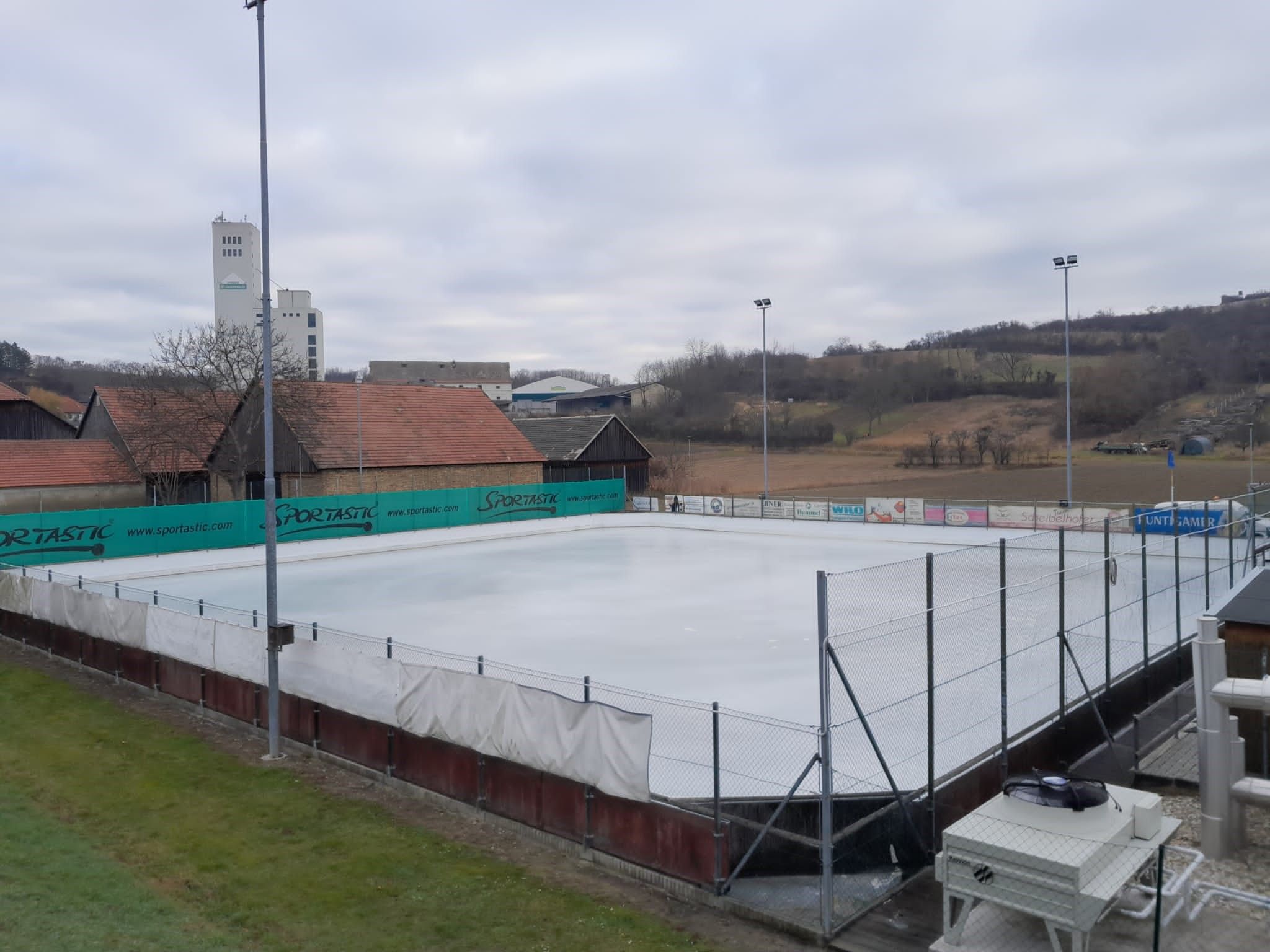 Egy üres jégpálya a környező épületekkel és dombokkal a háttérben.