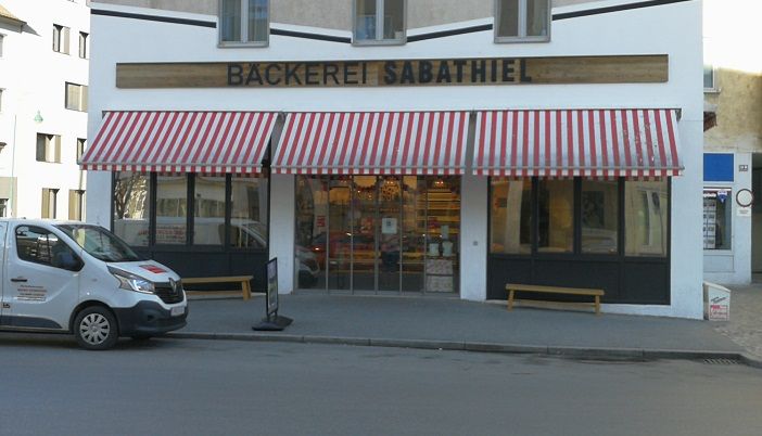 A Sabathiel pékség külső képe, piros-fehér csíkos napellenzővel és az előtte álló kiszállító kocsival.