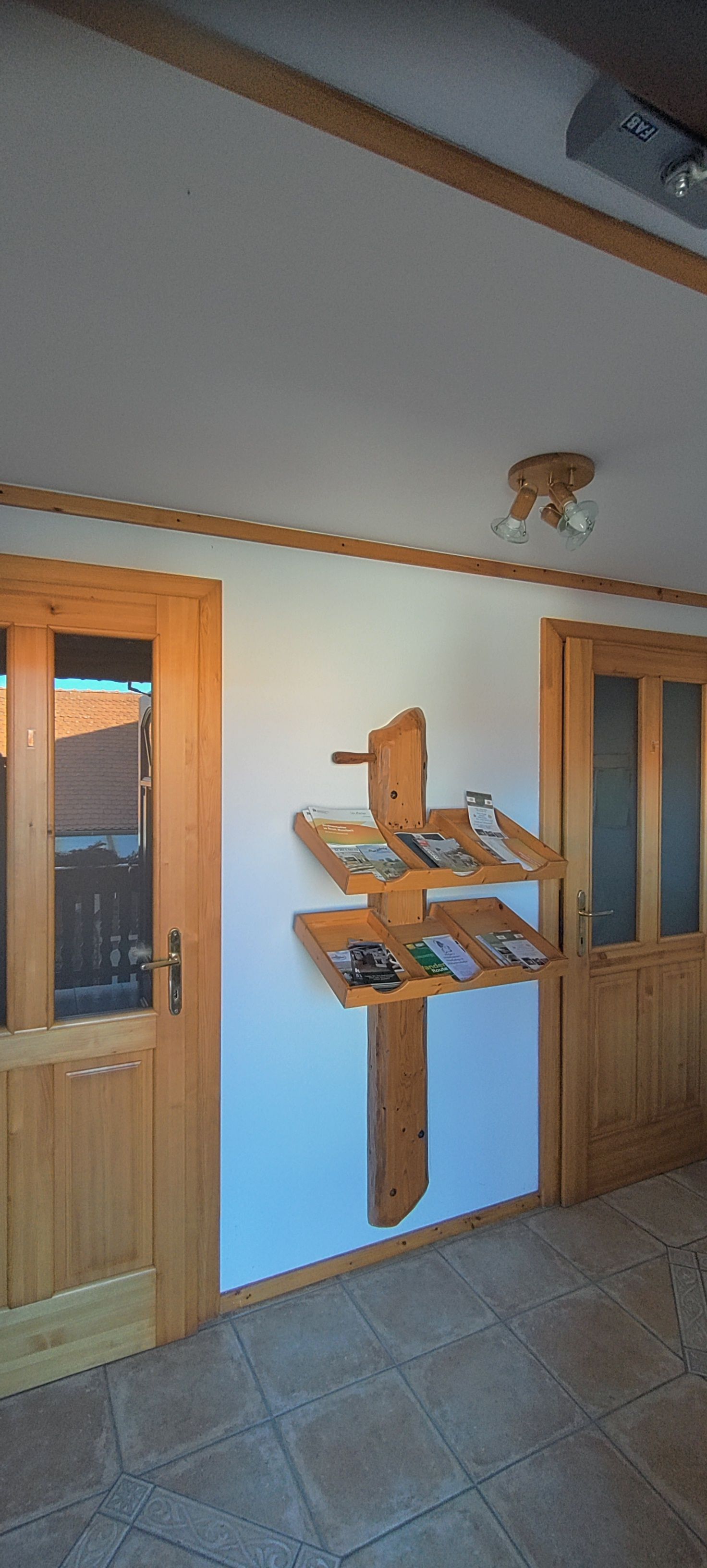 Egy fehér falon, két faajtó között egy fapolc brosúrákkal.