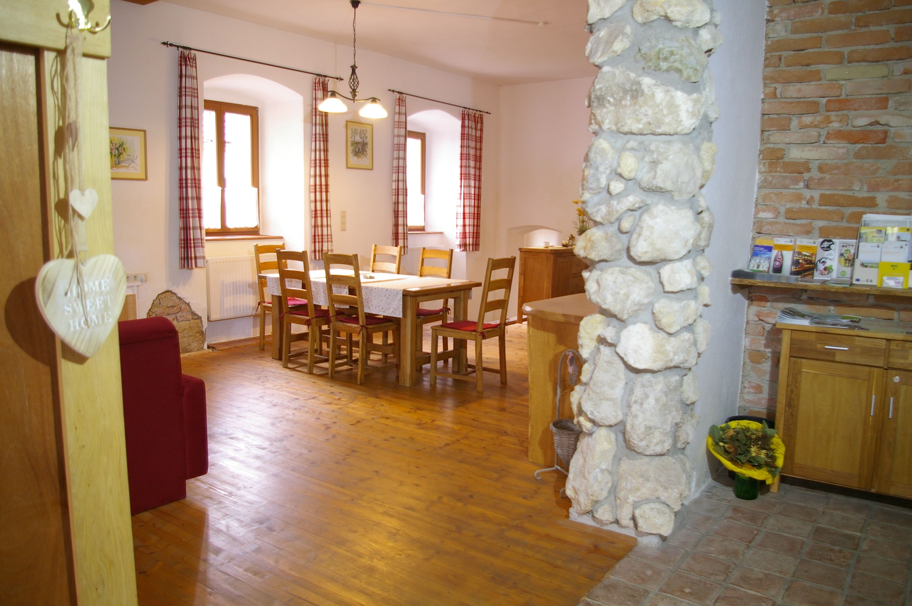 Hangulatos étkező, fa asztallal és székekkel, piros függönyökkel és kőfallal.