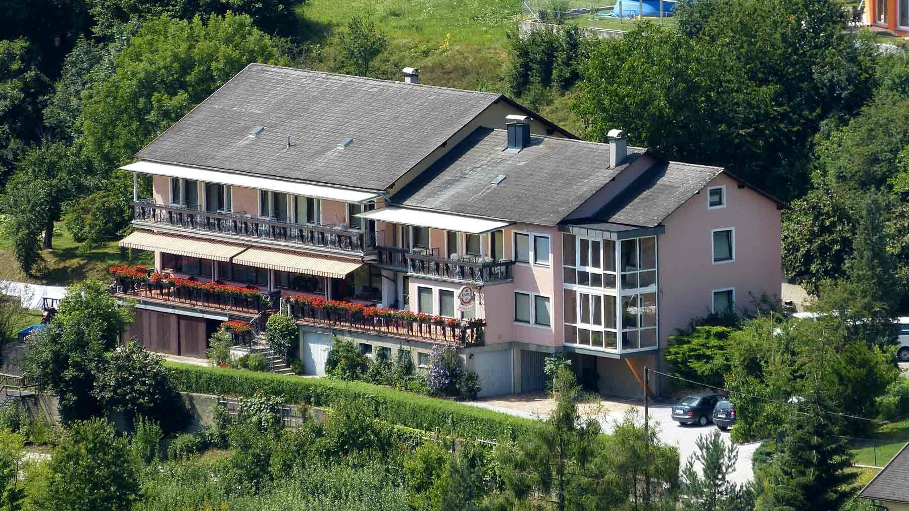 Nagy ház erkéllyel és kerttel, fákkal körülvéve.