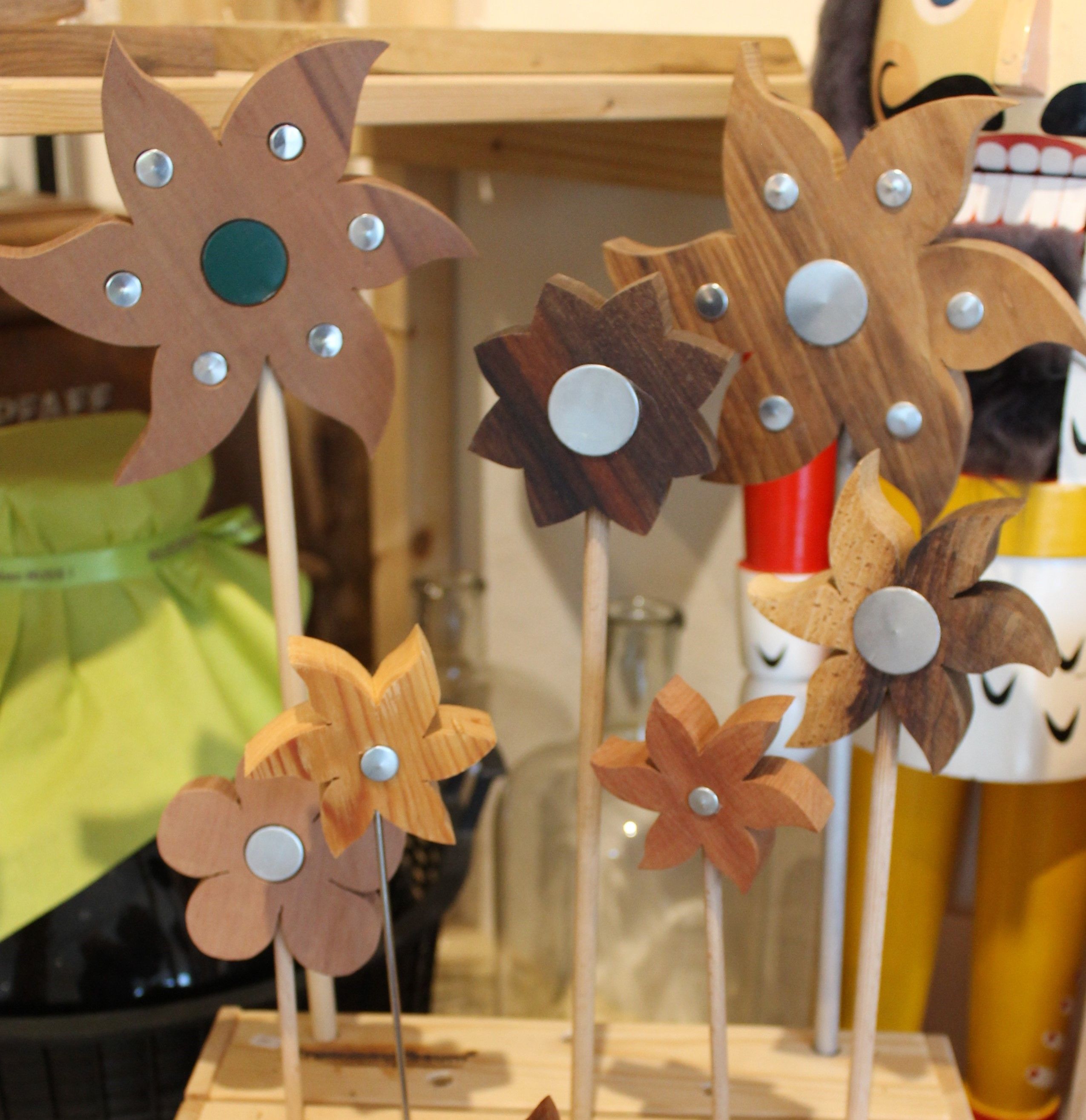 Fából készült virágok fémdíszítéssel rudakon egy polcon.