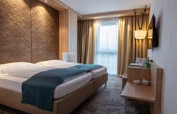 Modern szállodai szoba franciaággyal, faburkolattal és függönyös ablakokkal.