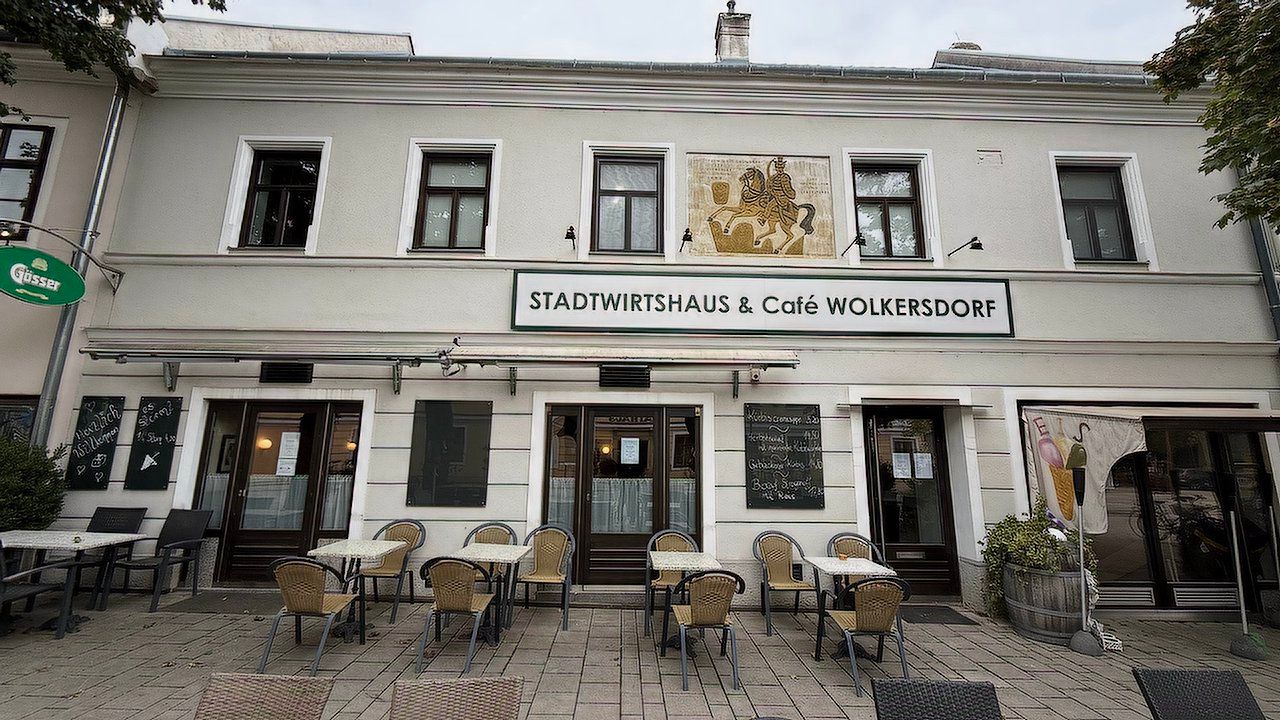 A Stadtwirtshaus & Café Wolkersdorf külső nézete a teraszon lévő asztalokkal és székekkel.