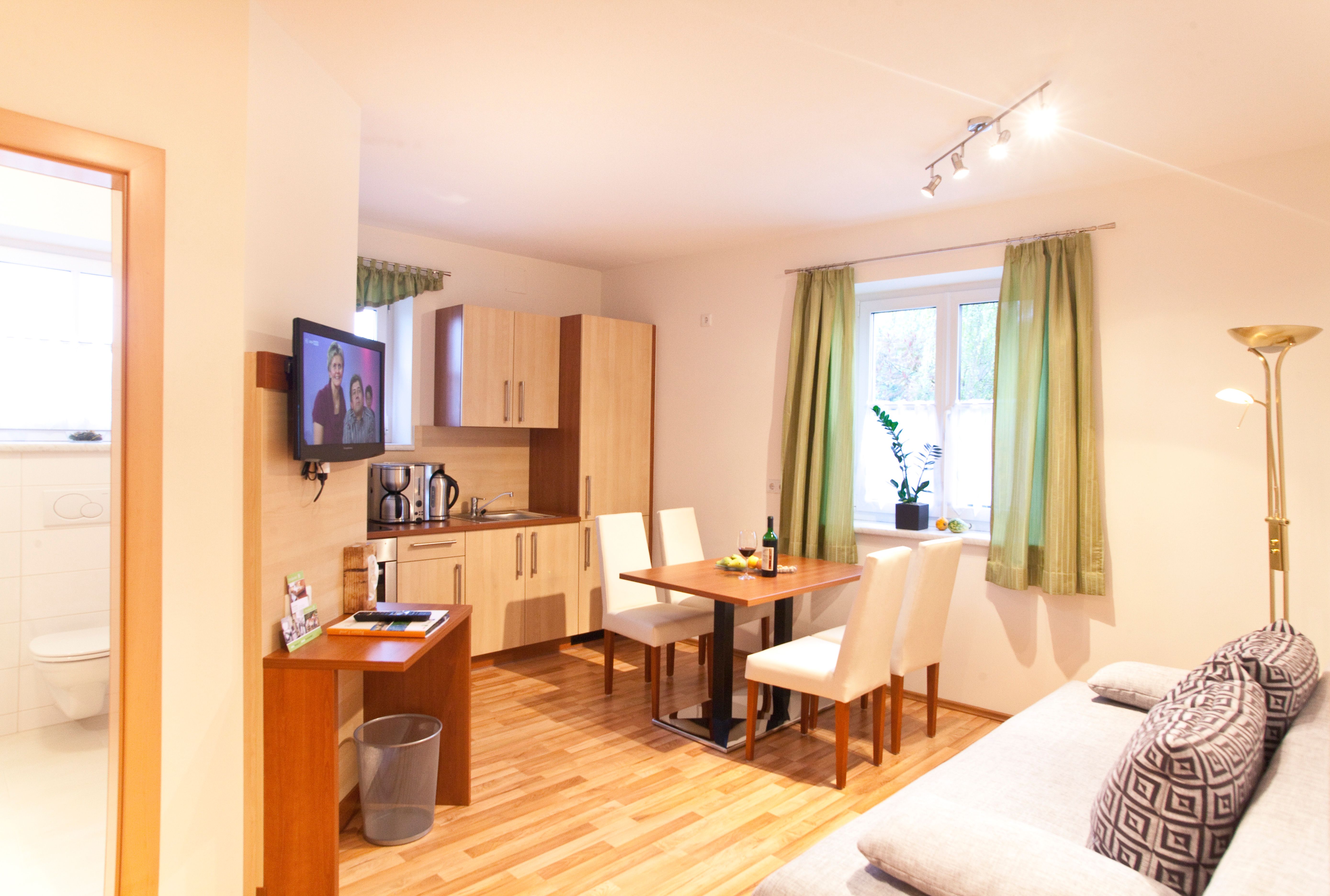 Modern konyha étkezőasztallal, kanapéval és TV-vel egy világos szobában.