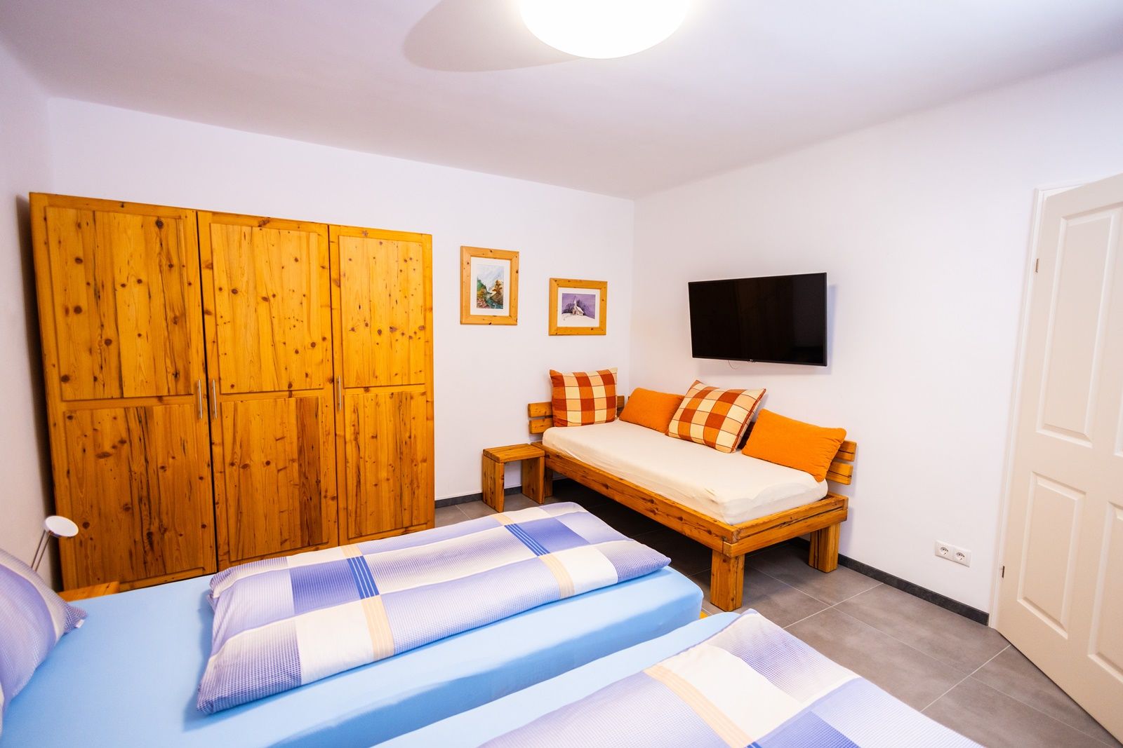 Hálószoba fából készült bútorokkal, két ággyal, kanapéval, TV-vel és faliképekkel.