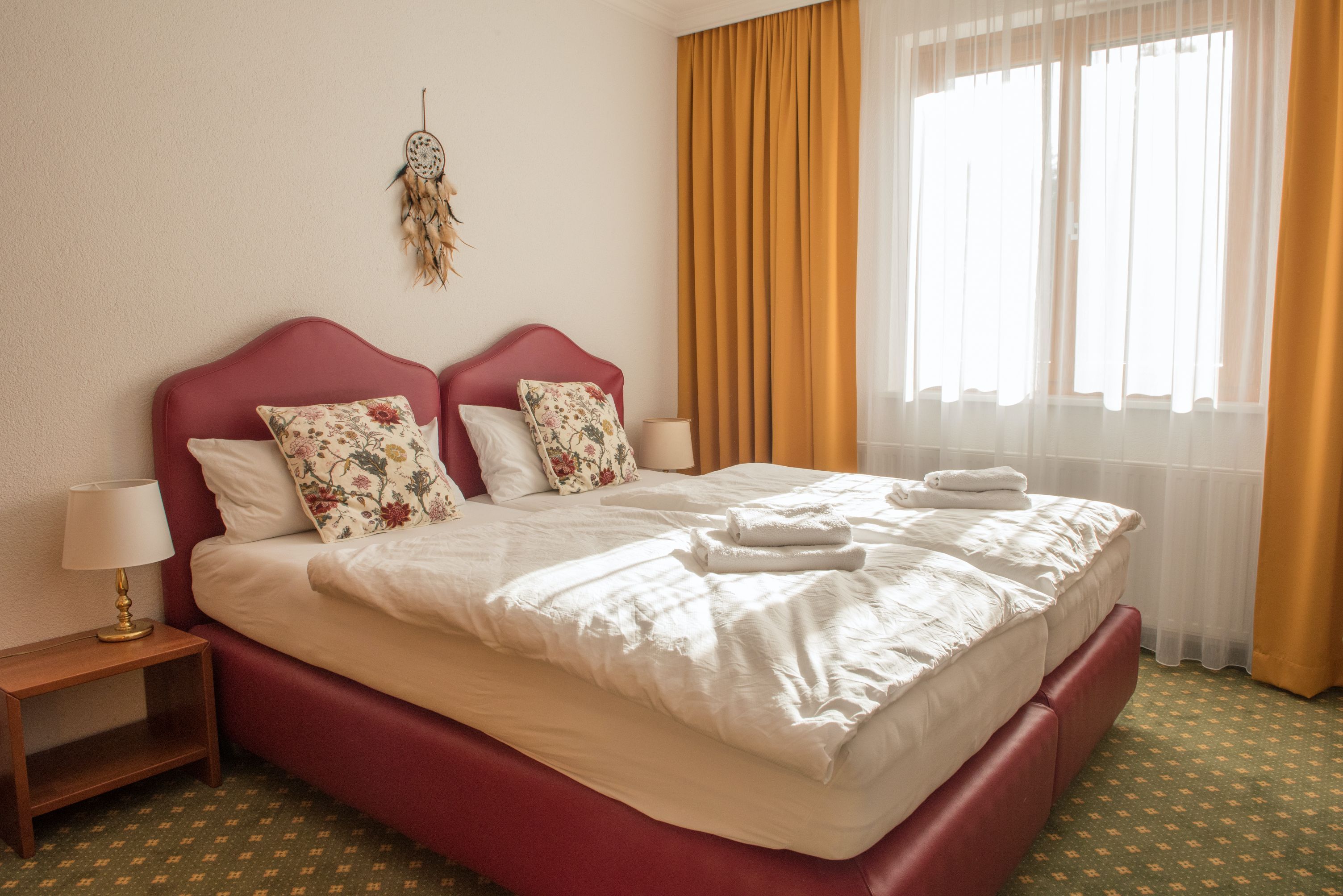 Hangulatos kétágyas szoba két ággyal, sárga függönyökkel és egy álomfogóval a falon.