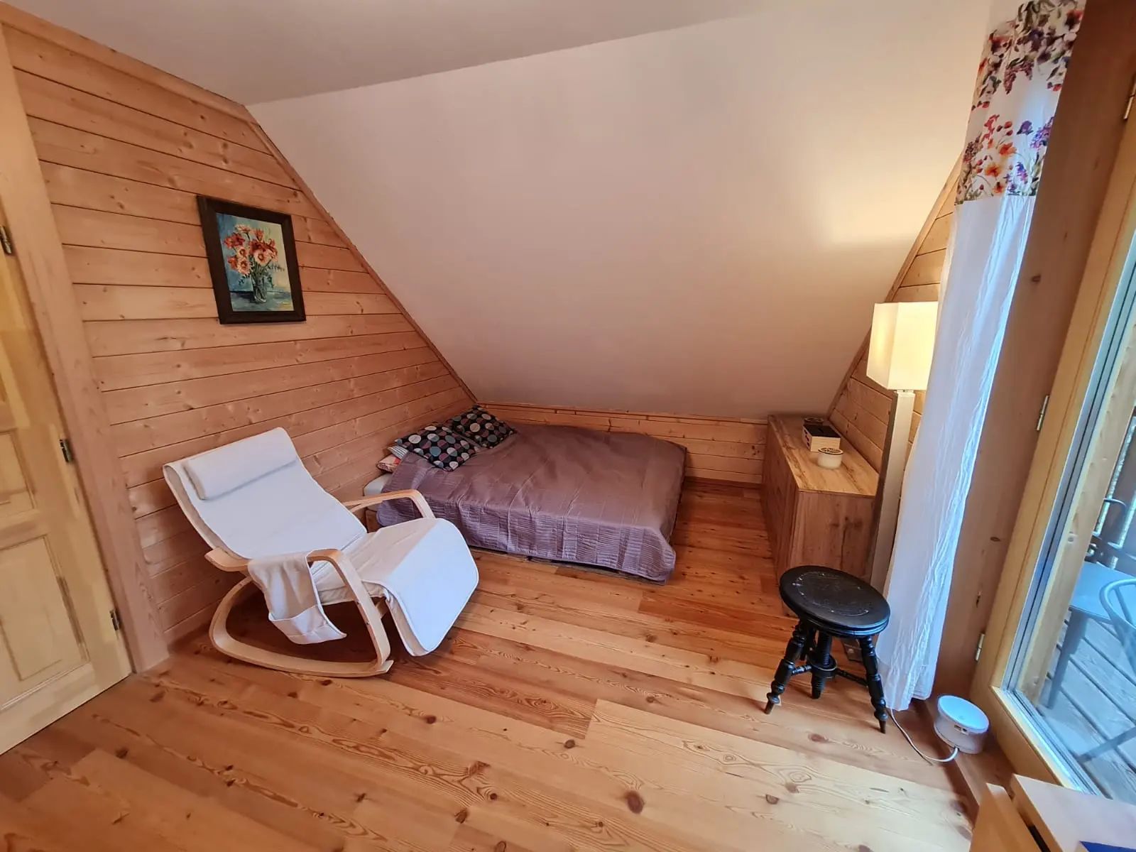 Hangulatos szoba fából készült falakkal, ággyal, fehér hintaszékkel és kis asztallal.