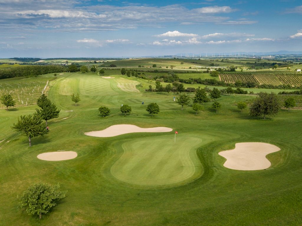 Egy golfpálya légifelvétele zöld területekkel, homokbunkerekkel és a környező mezőkkel.