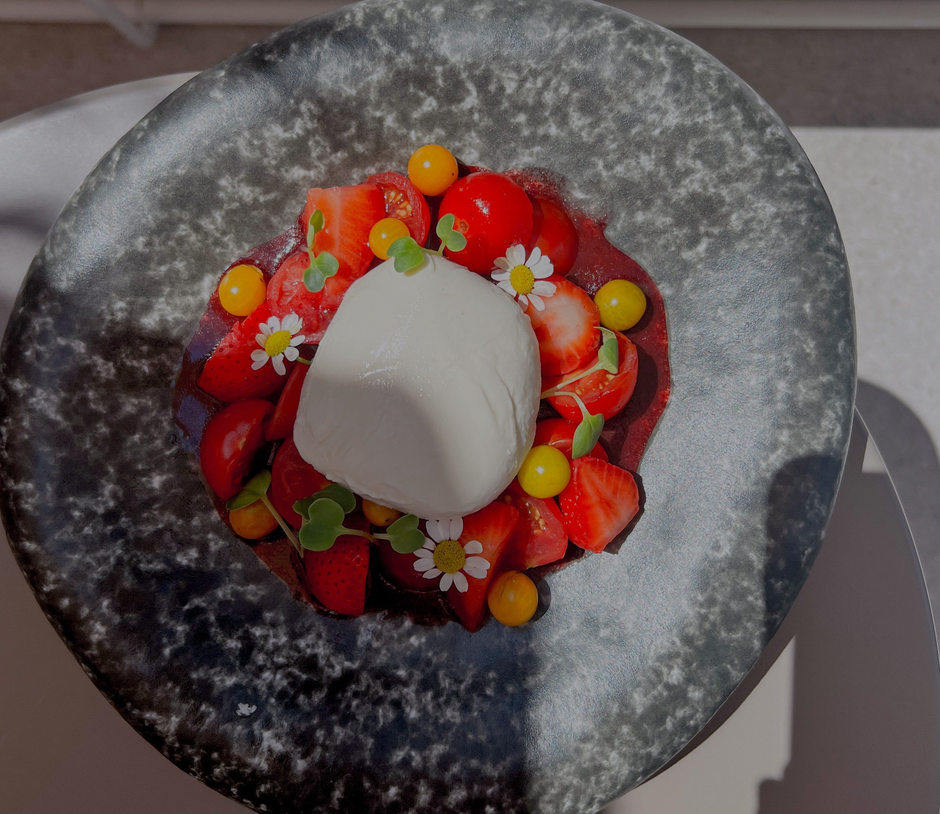 Egy tányér burrata, eper, paradicsom és ehető virágok.
