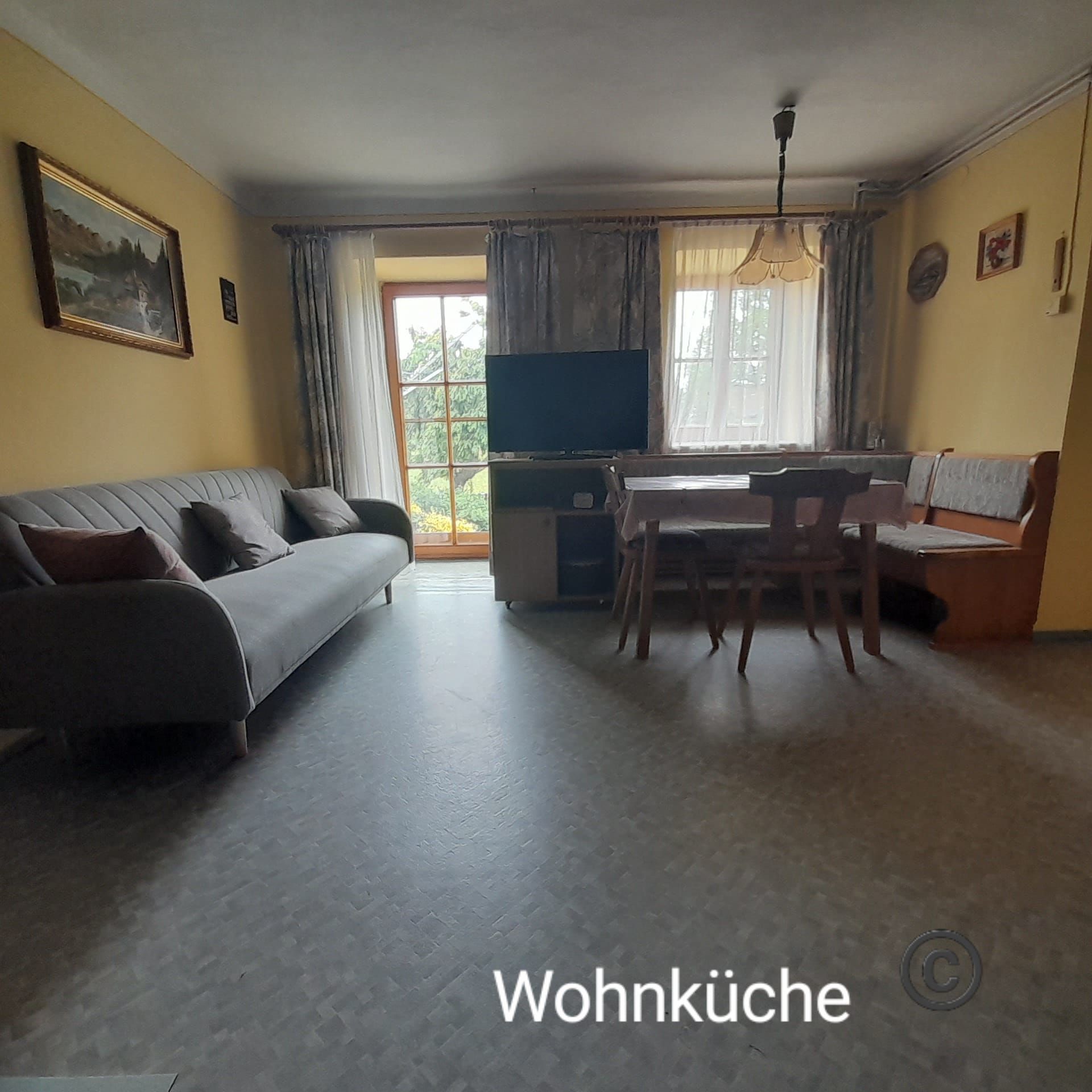 Nappali-konyha kanapéval, étkezőasztallal és TV-vel a nagy ablakok előtt.