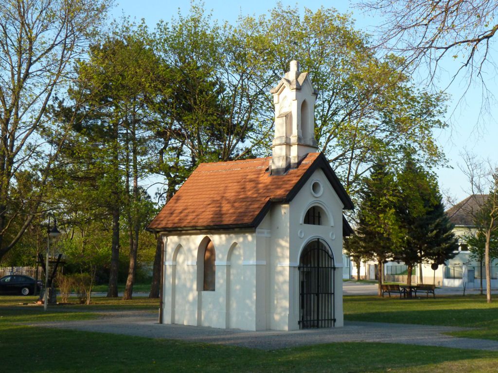 Egy kis fehér kápolna piros tetővel egy fákkal körülvett parkban.