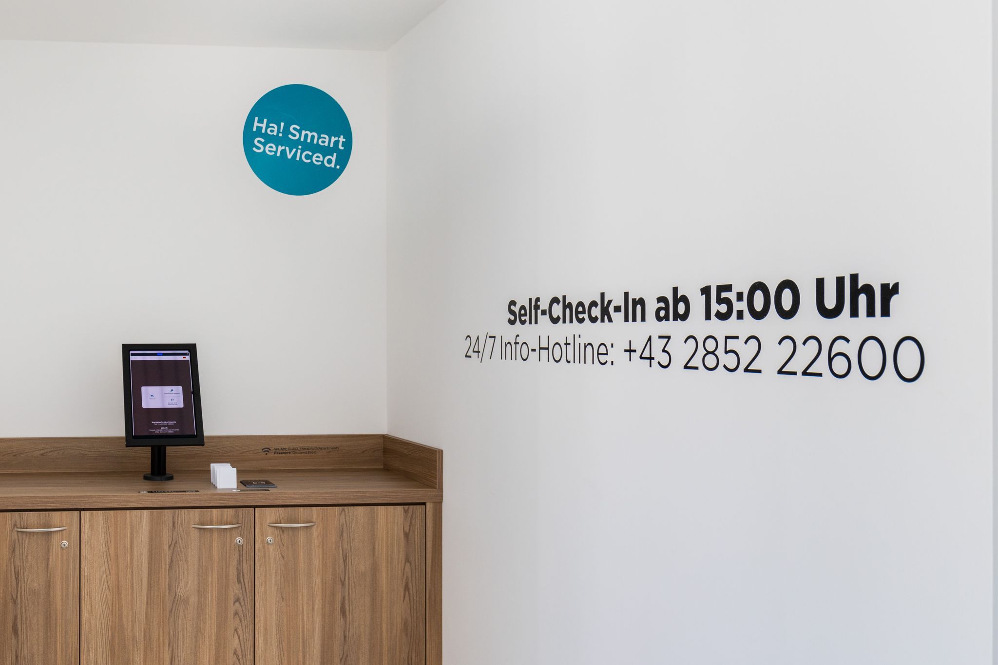 Egy önálló bejelentkezési terület, ahol egy képernyő és a falon feltüntetett, éjjel-nappal elérhető forróvonal telefonszáma található.