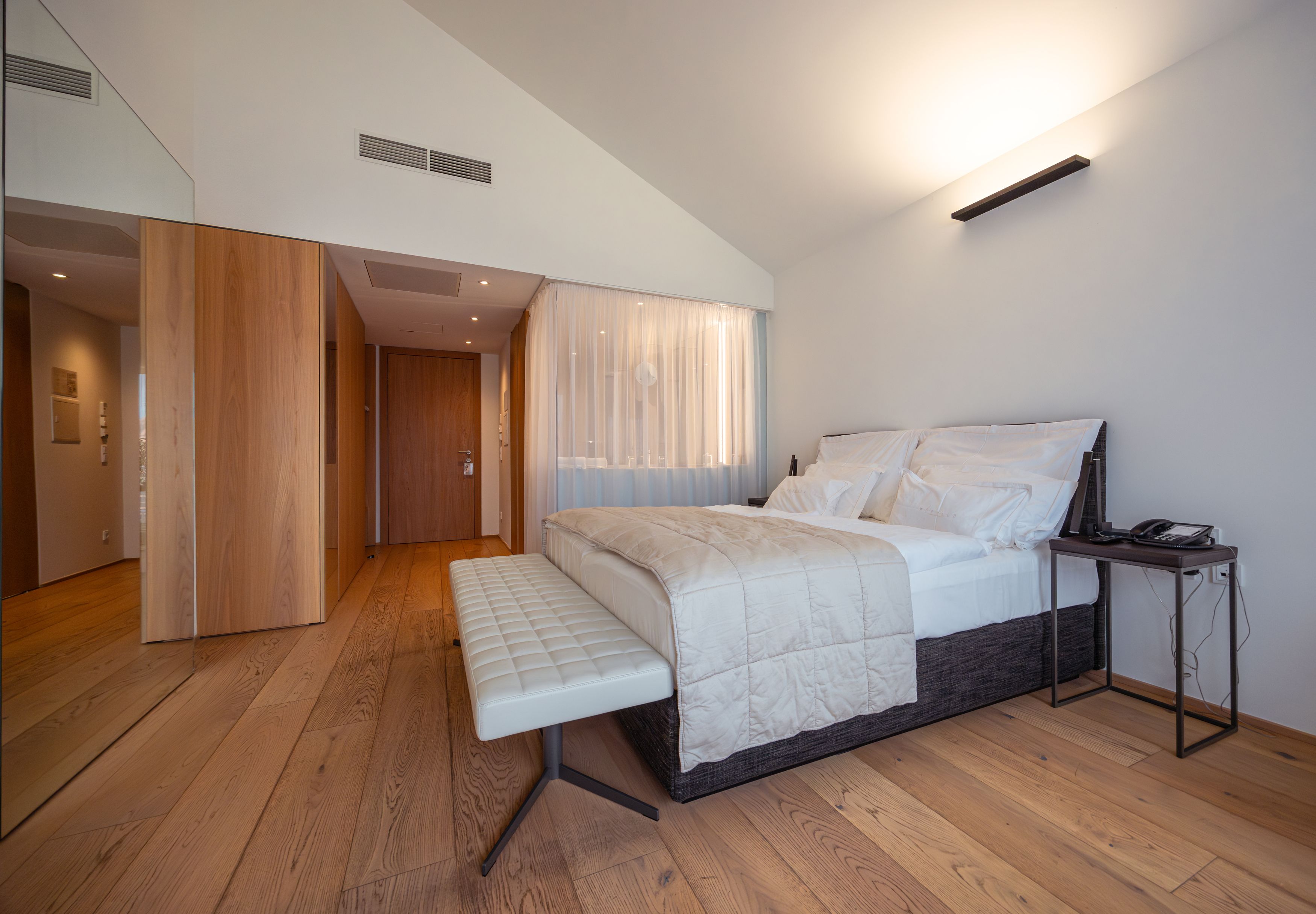 Modern szállodai szoba nagy ággyal, fapadlóval és minimalista berendezéssel.