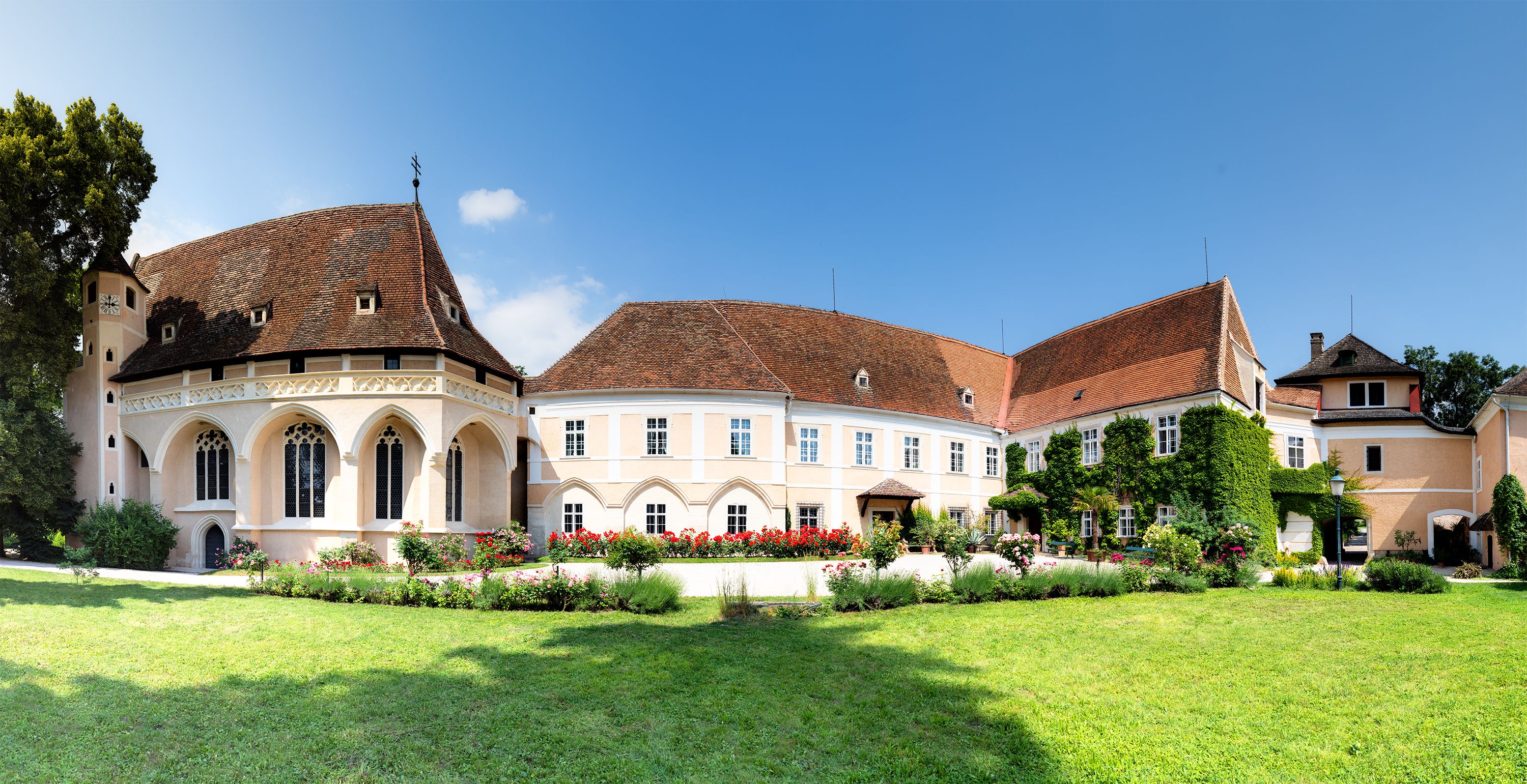 A Schrattenthal-kastély panorámaképe, előtérben ápolt kert és virágzó rózsák.