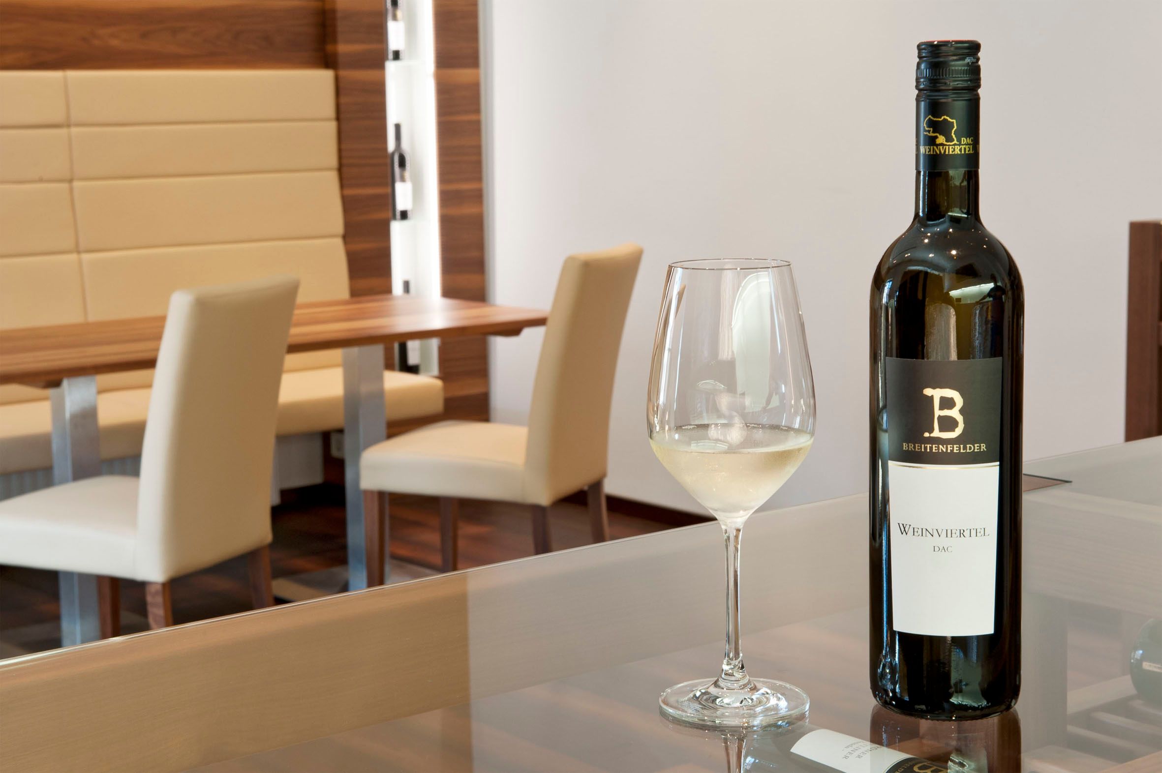 Egy kóstolóterem, egy üveg fehérborral és egy teli borospohárral az asztalon.