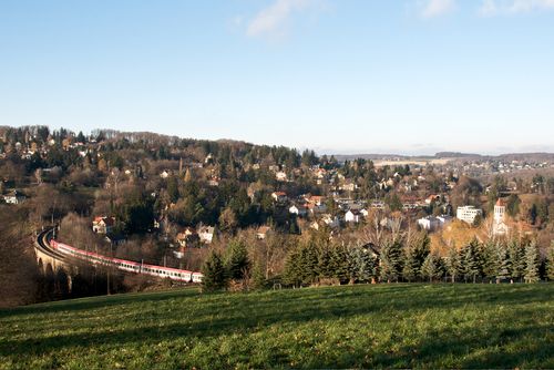 Tájkép vonattal a viadukton Eichgrabenben, dombok és házak között.