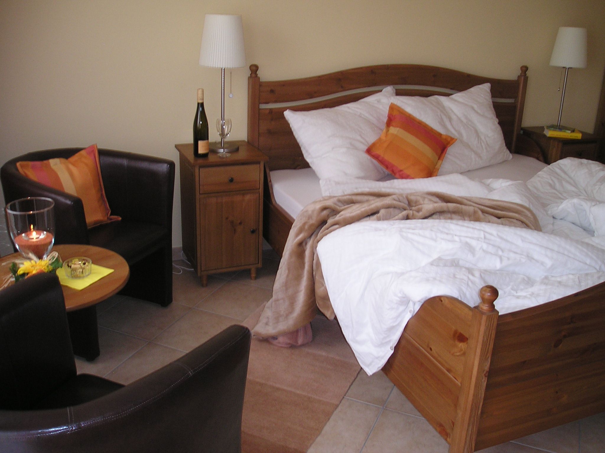 Hangulatos vendégszoba franciaággyal, éjjeliszekrénnyel, lámpával, karosszékkel és asztallal.