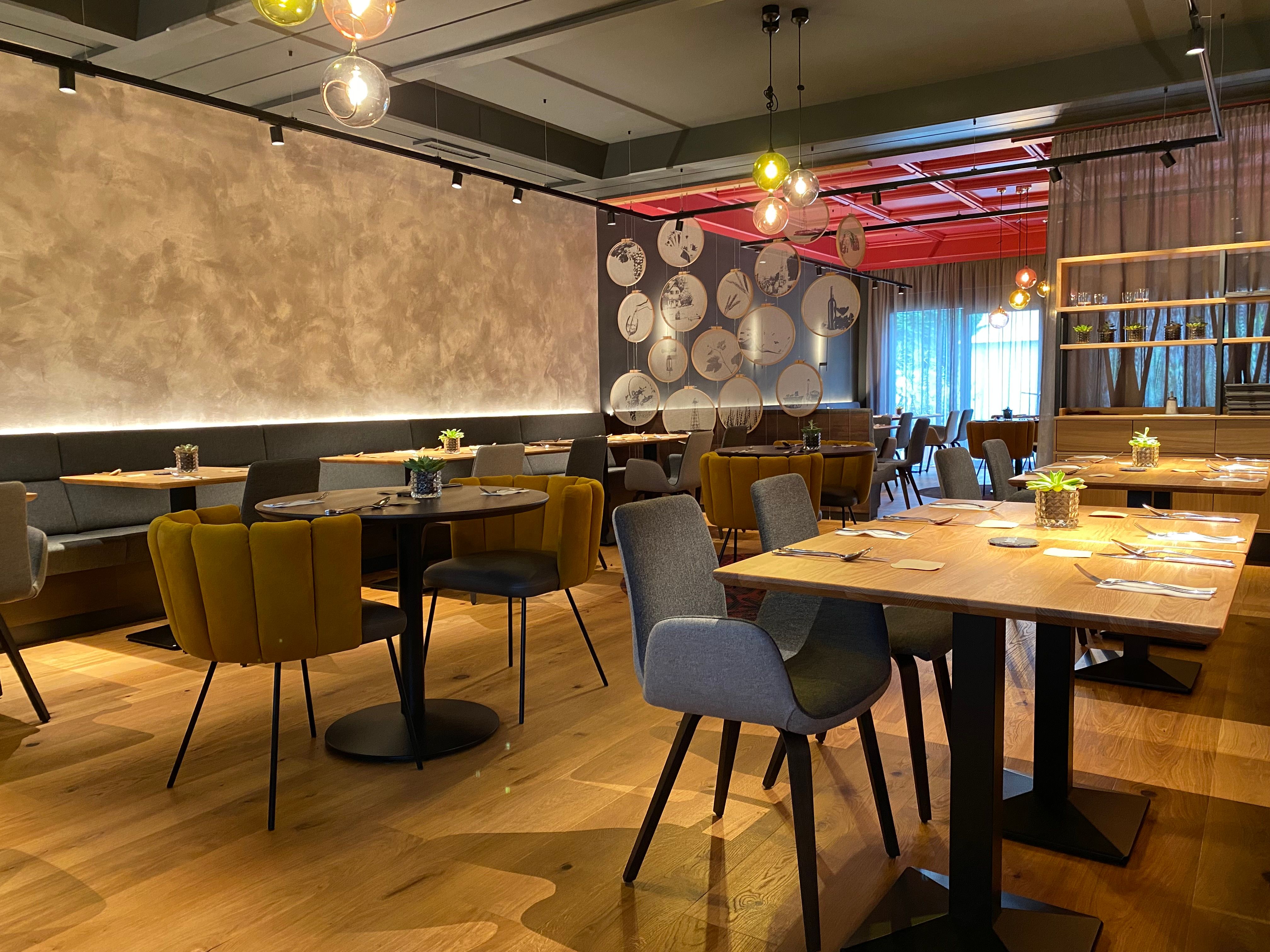 Modern étterem elegáns berendezéssel, fa asztalokkal és hangulatos székekkel.