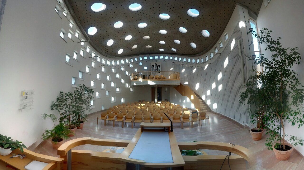 Modern templombelső kerek ablakokkal és fa bútorokkal.