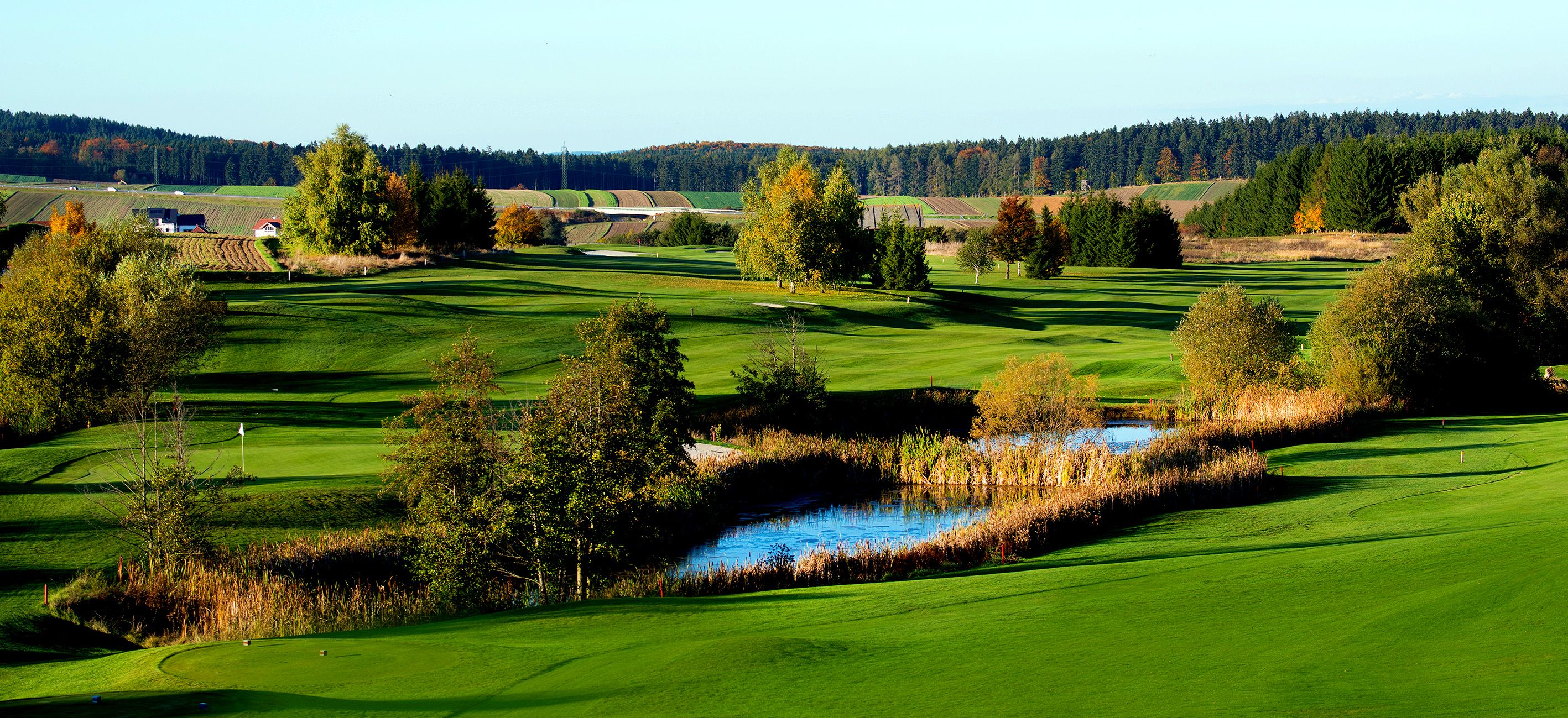Zöld golfpálya táj tóval és fákkal ősszel.