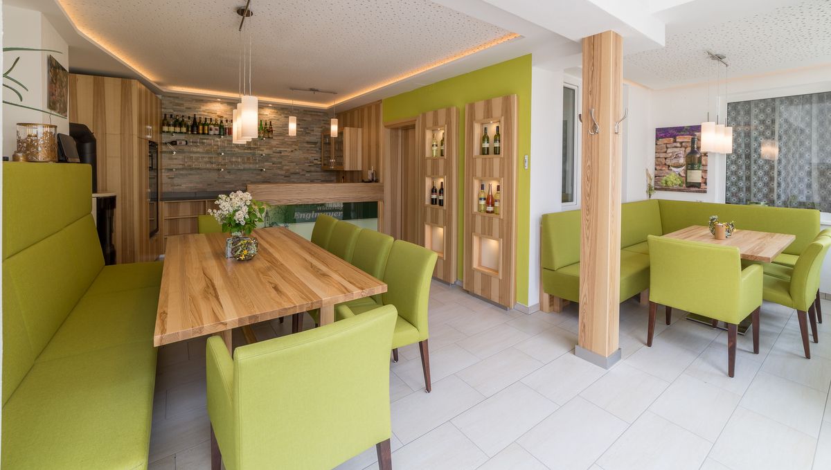 Modern kóstolóterem fa asztalokkal és zöld kárpitozott bútorokkal.