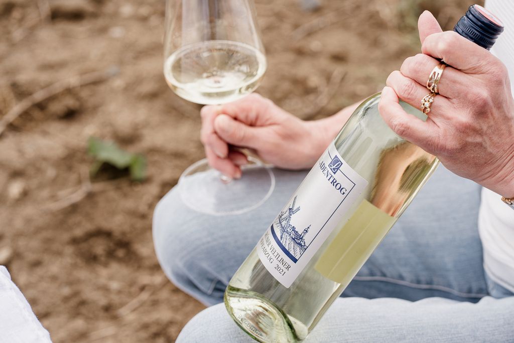 Személy kezében egy üveg bor és egy pohár fehérbor.