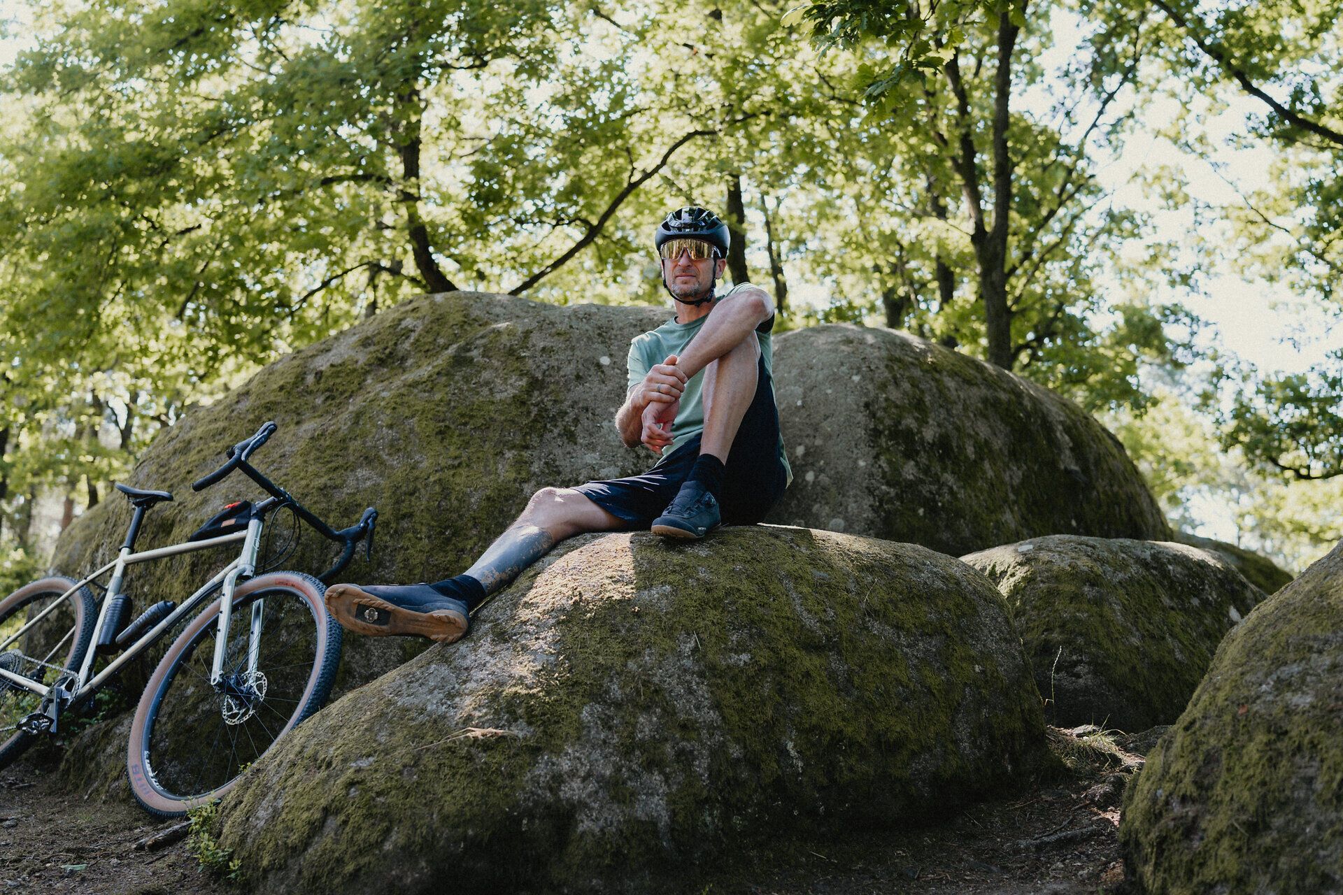 Ein Mann in Fahrradoutfit und Helm sitzt auf einem Stein und genießt den Augenblick. Neben ihm sein Fahrrad an einem weiteren Stein angelehnt. 