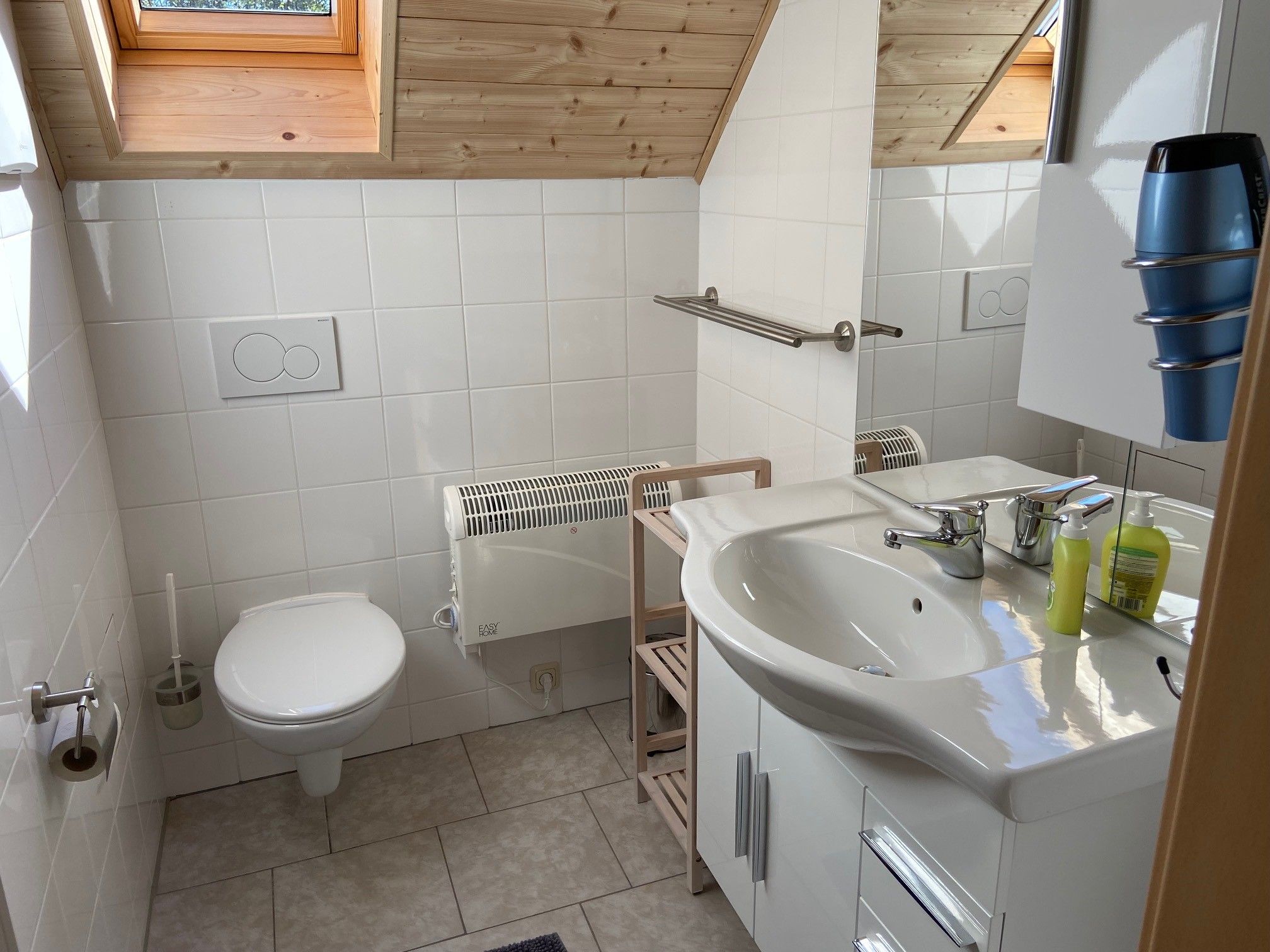 Modern fürdőszoba tetőablakkal, mosdóval, WC-vel és törölközőtartóval.