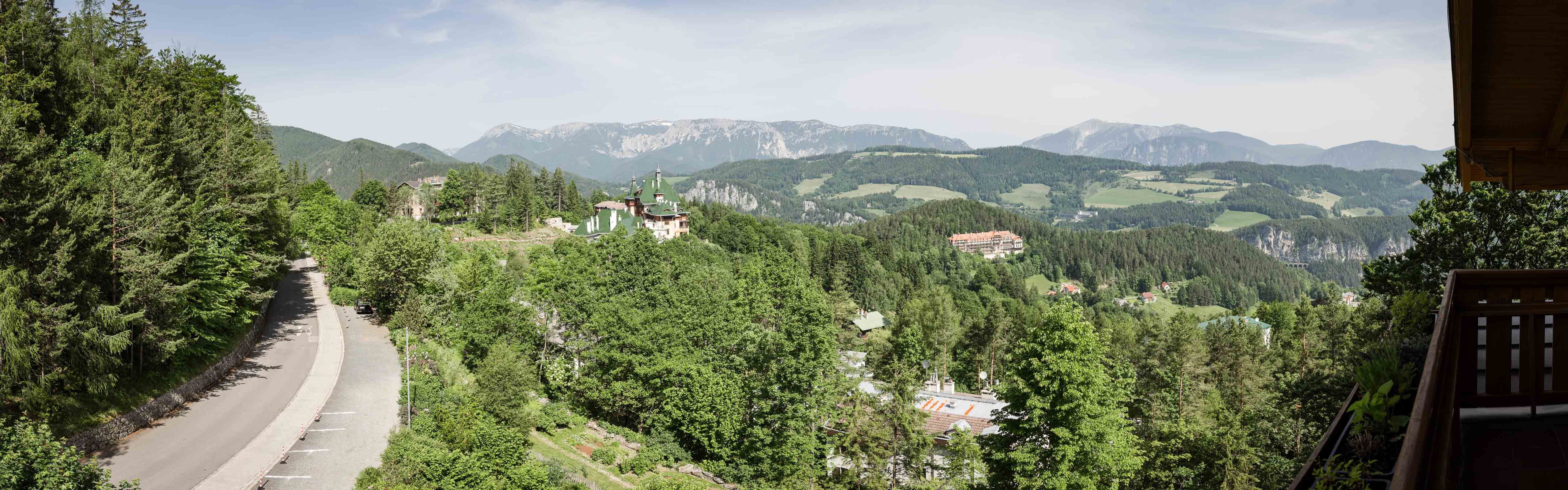 Hegyvidéki táj panorámaképe erdővel, úttal és épületekkel.