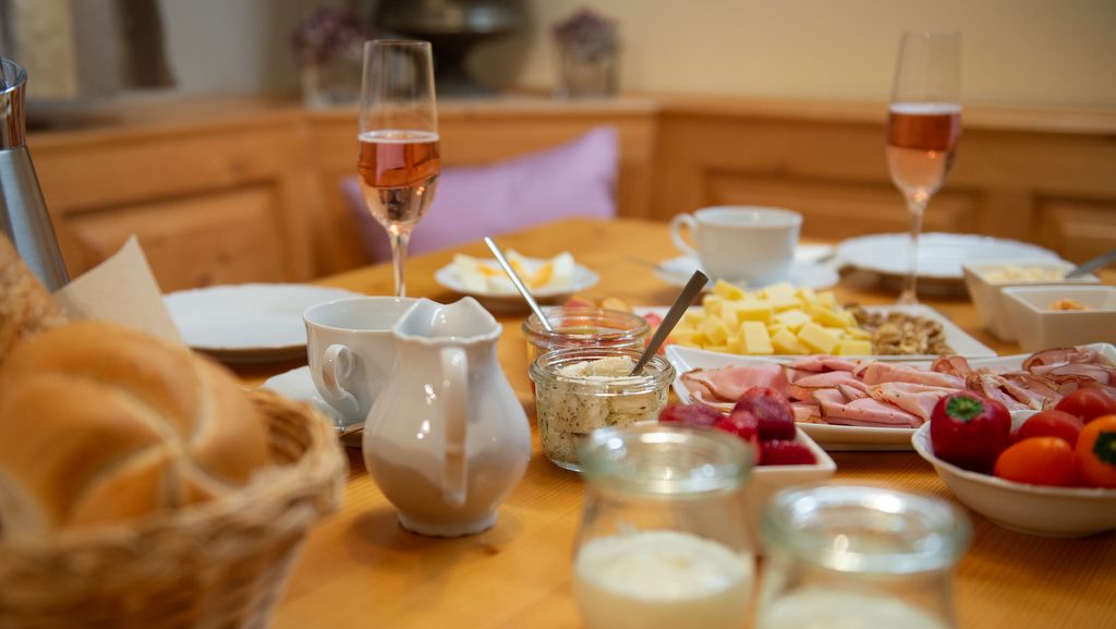 Reggelizőasztal zsemlével, felvágottal, sajttal, pohár pezsgővel és joghurttal.