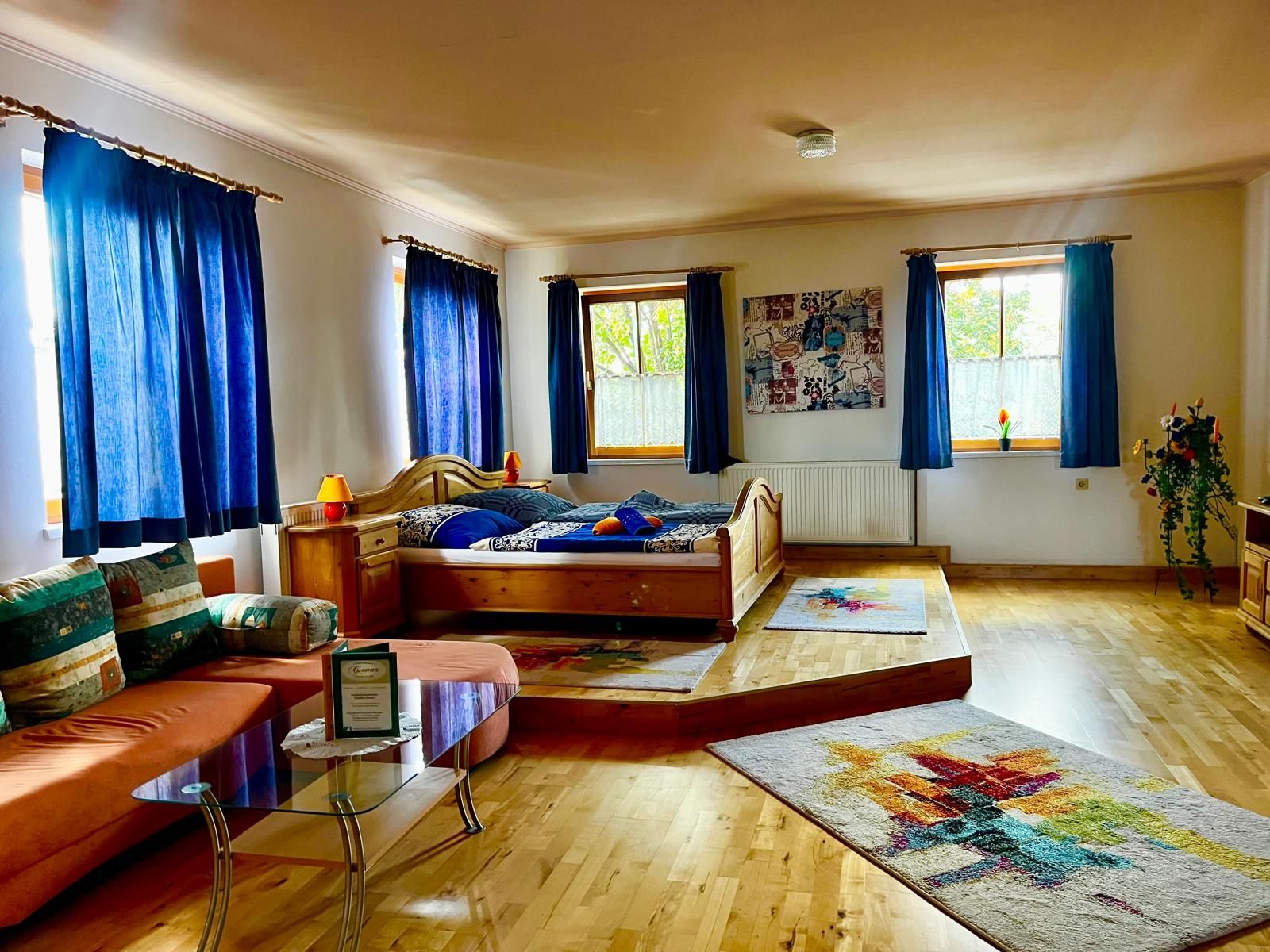 Hangulatos szoba fapadlóval, franciaággyal, kanapéval és kék függönyökkel.