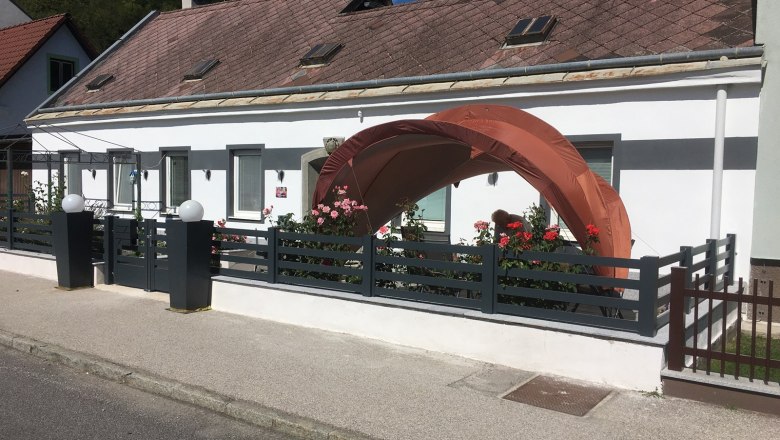 Feh&eacute;r h&aacute;z, kis kerttel &eacute;s egy narancss&aacute;rga sz&iacute;nű pavilonnal az ajt&oacute; előtt.