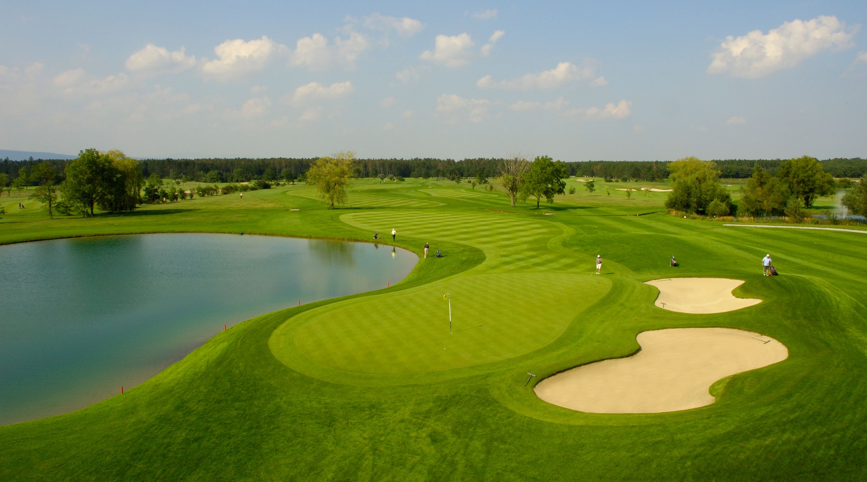 Golfpálya tóval, homokbunkerrel és játékosokkal.