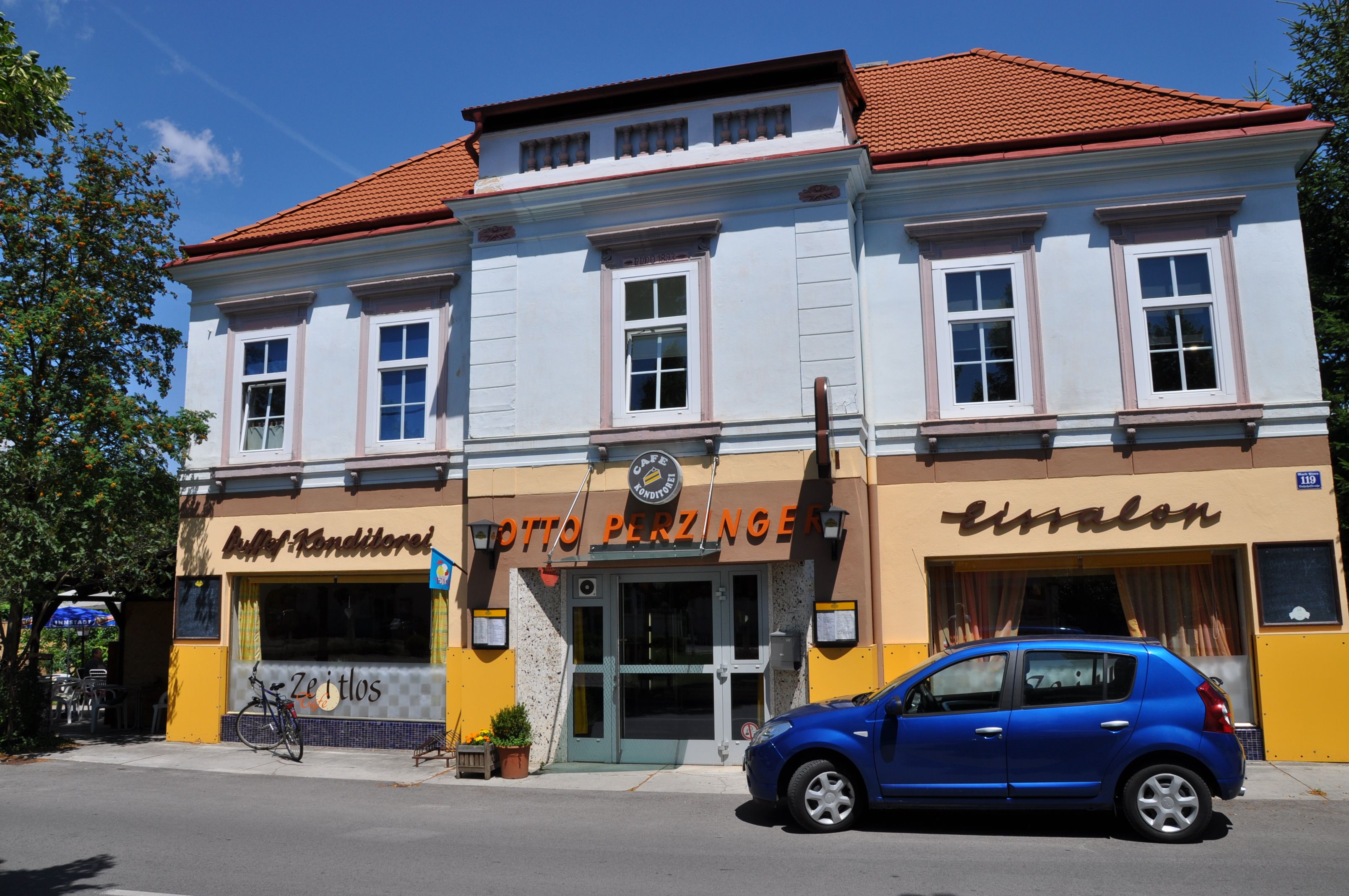 Egy kék homlokzatú, piros tetejű kávézó külső nézete, előtte egy kék autó parkol.