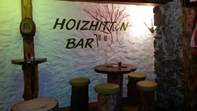 Rusztikus b&aacute;r, fab&uacute;torokkal &eacute;s "Hoizhitt'n Bar" felirattal a falon.