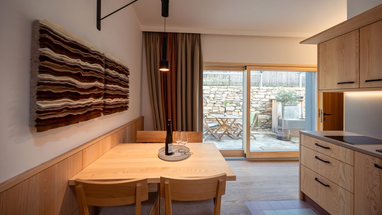 Egy modern &eacute;tkező belső n&eacute;zete, fa b&uacute;torokkal &eacute;s falik&eacute;pekkel, kil&aacute;t&aacute;s a teraszra egy &uuml;vegajt&oacute;n kereszt&uuml;l.