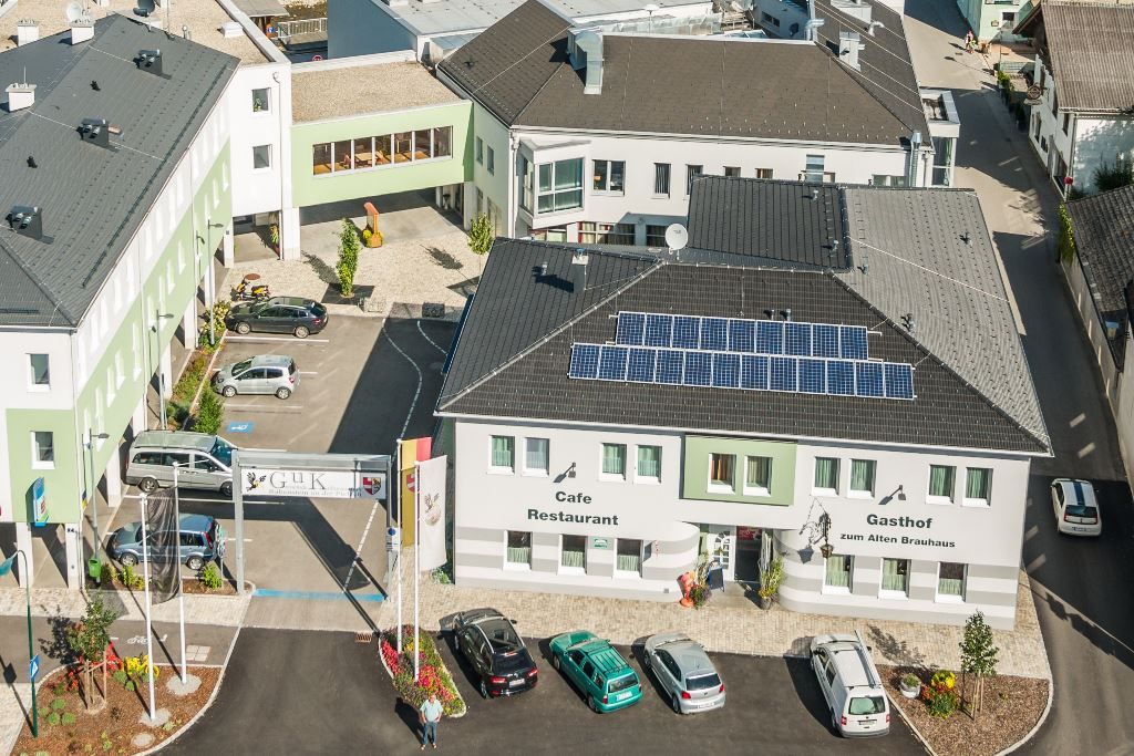 Légi felvétel egy épületkomplexumról a Gasthof zum Alten Brauhaus épületével, napelemekkel a tetőn és több parkoló autóval.