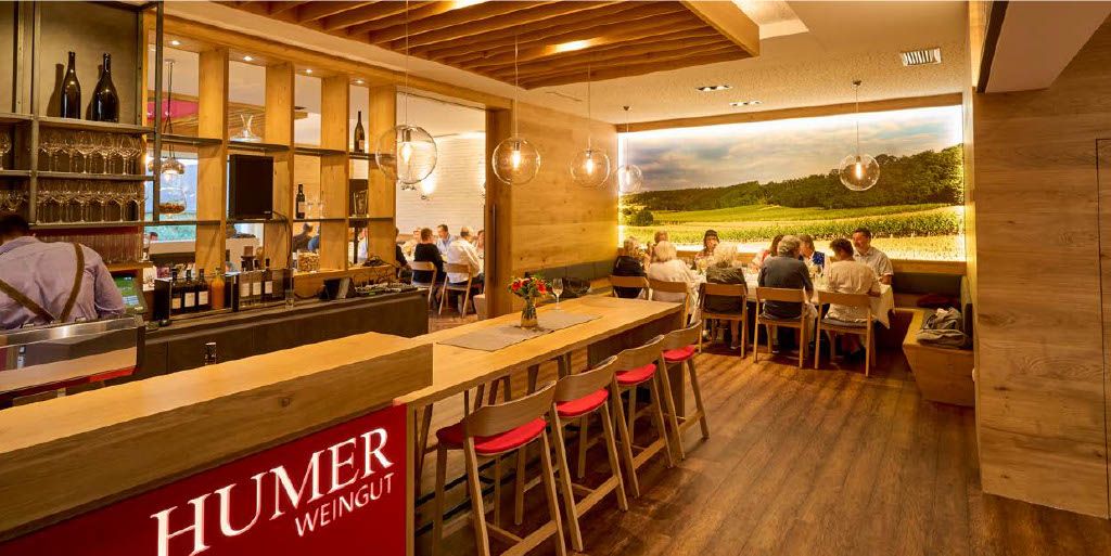 Egy modern borozó belső nézete, fa bútorokkal és egy nagyméretű fotótapétával egy szőlőskertről.