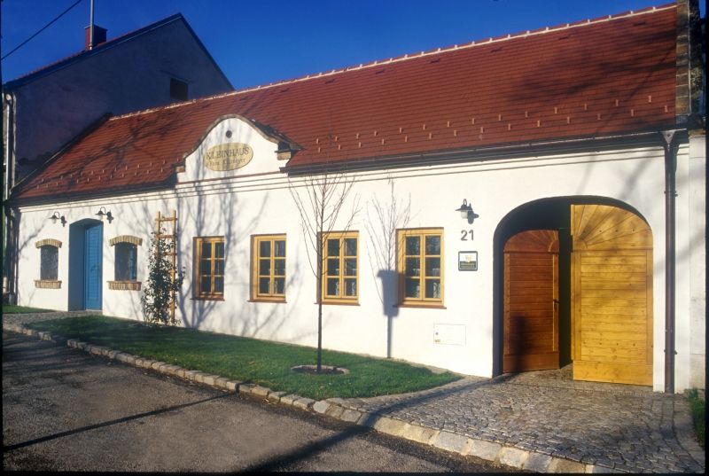 Fehér épület piros tetővel és faajtókkal, felirattal: "Kleinhaus".