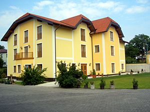 Sárga kétszintes épület piros tetővel és gondozott kerttel.