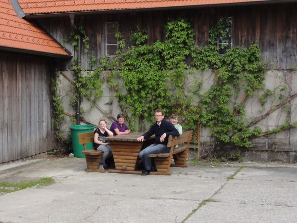 Négy ember ül egy faasztalnál egy borostyánnal benőtt épület előtt.