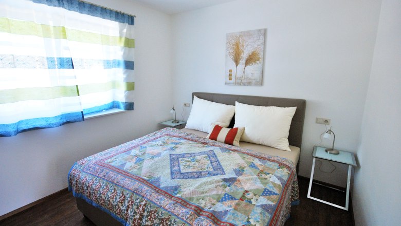 Egy h&aacute;l&oacute;szoba francia&aacute;ggyal, sz&iacute;nes &aacute;gytakar&oacute;val, k&eacute;t &eacute;jjeliszekr&eacute;nnyel &eacute;s egy cs&iacute;kos f&uuml;gg&ouml;ny&ouml;s ablakkal.