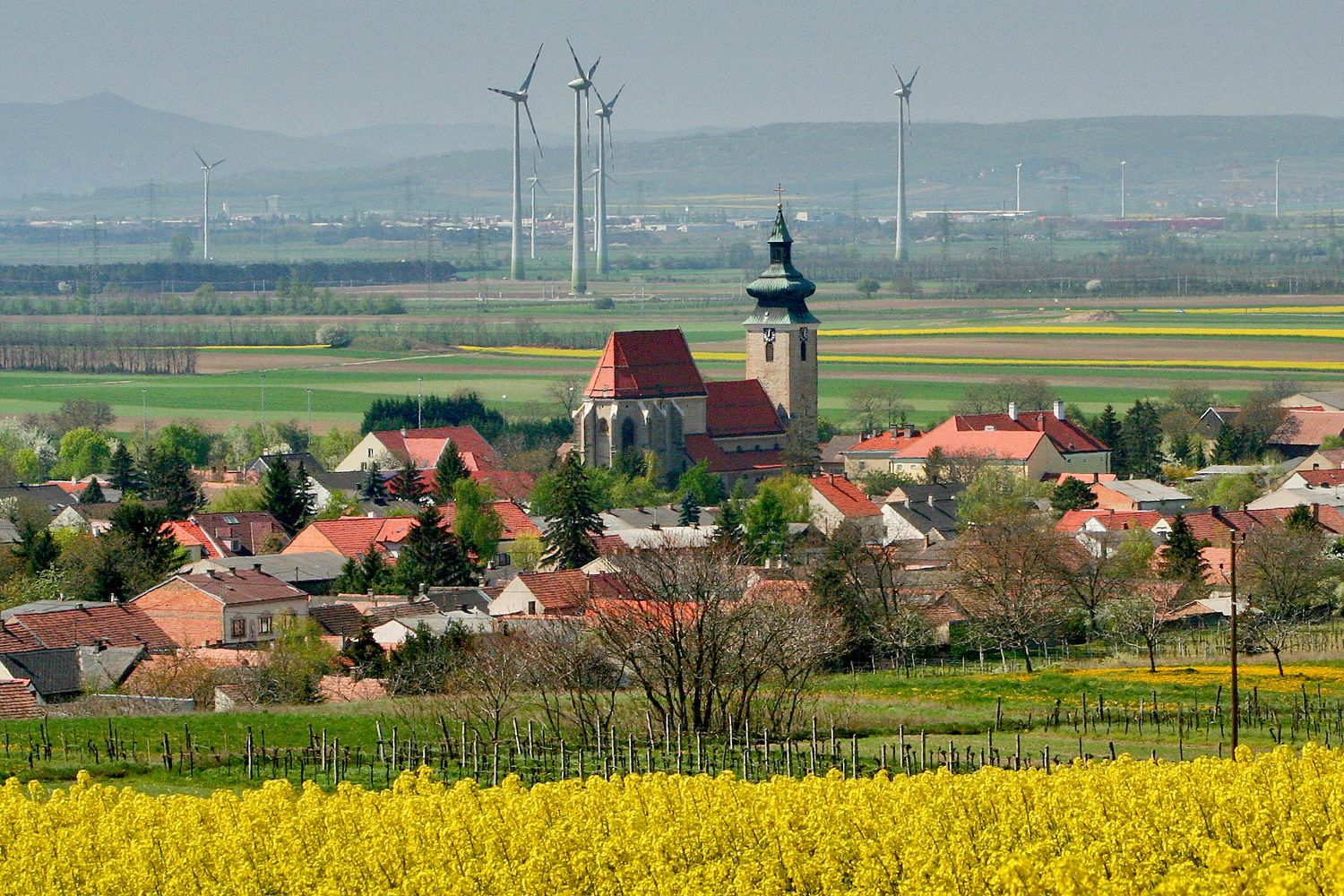 Pillichsdorf látképe a templommal, a háttérben mezőkkel és szélturbinákkal.