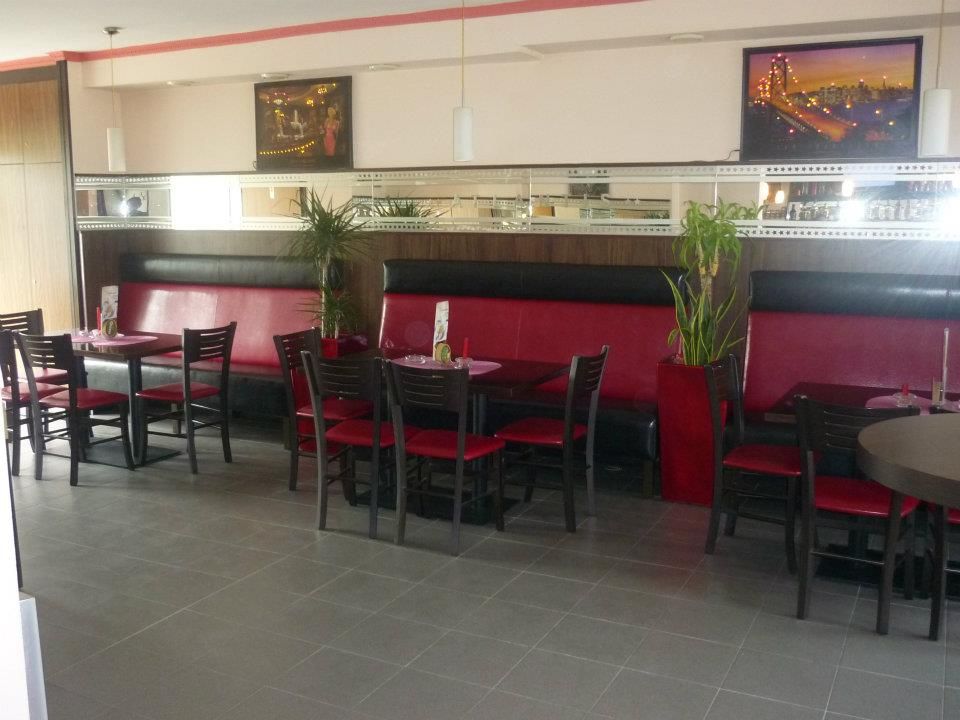 Egy kávézó belső nézete piros padokkal és fekete székekkel.