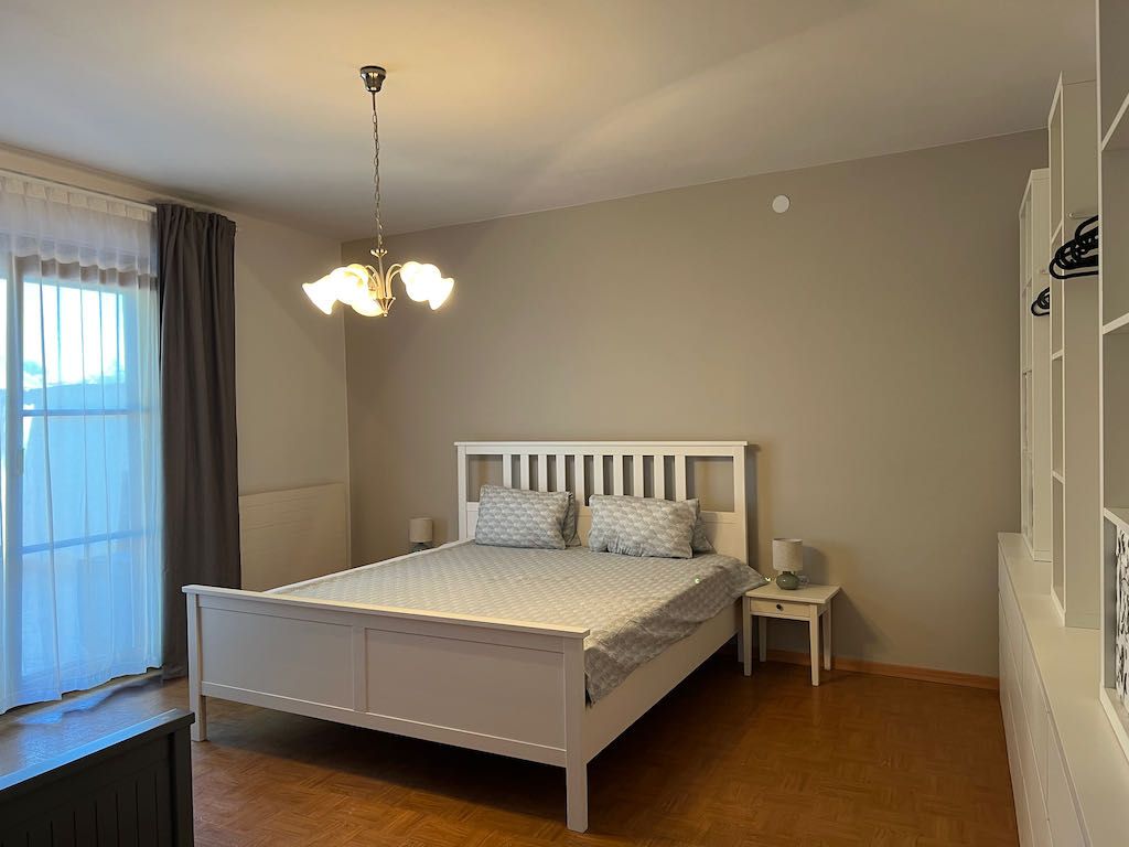 Hálószoba fehér ággyal, éjjeliszekrénnyel és szekrénnyel.