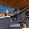 Egy modern épület belső udvara fa elemekkel, üvegkorláttal és szürke ülőbútorokkal.