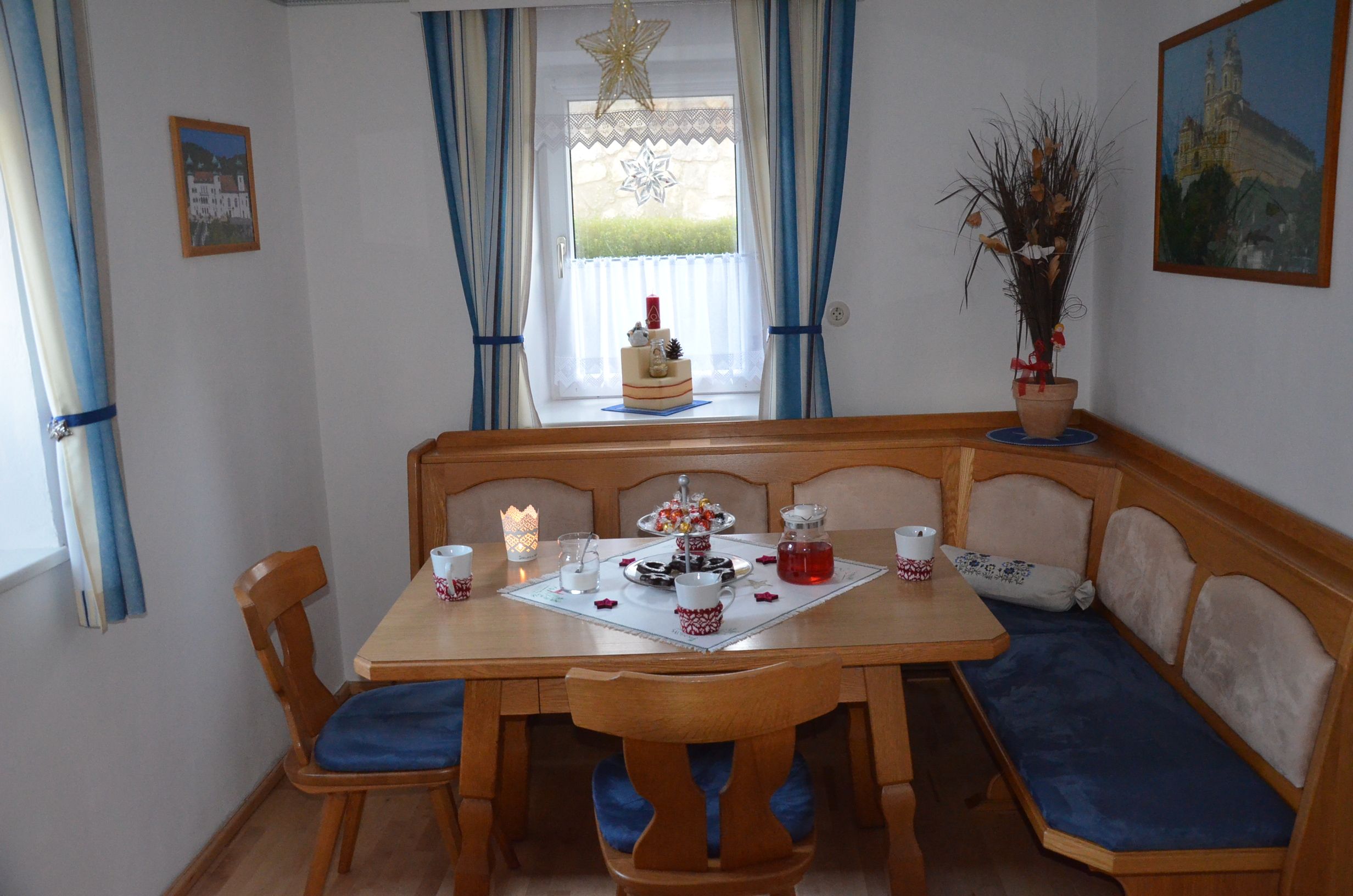 Hangulatos étkező, fa asztallal, sarokpaddal és kék kárpittal. Ablak kék függönyökkel és karácsonyi díszekkel.